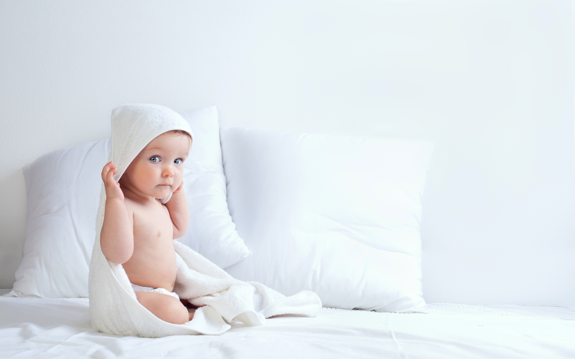 Грудной ребенок сидит на кровати с подушками