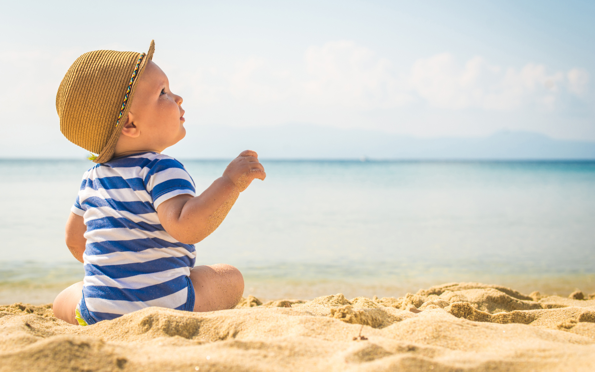 Маленький ребенок сидит на песке на пляже у моря