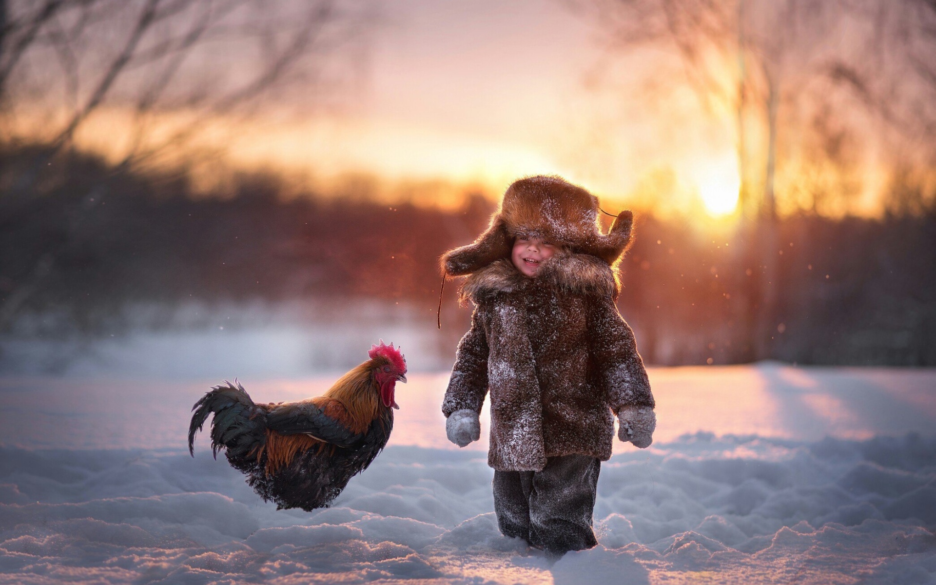 Маленький мальчик с петухом на снегу зимой