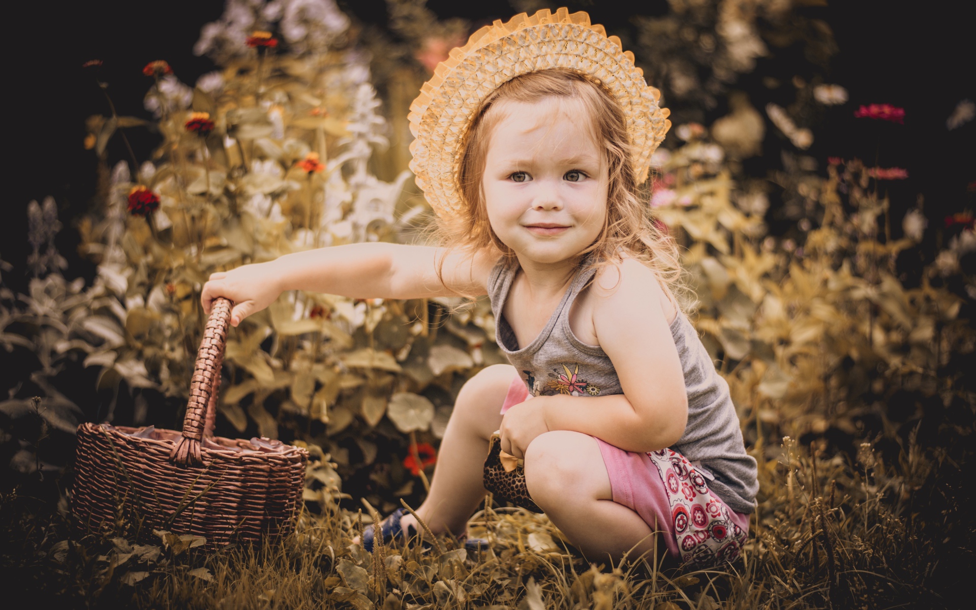 Маленькая девочка в шляпе сидит на траве с корзиной