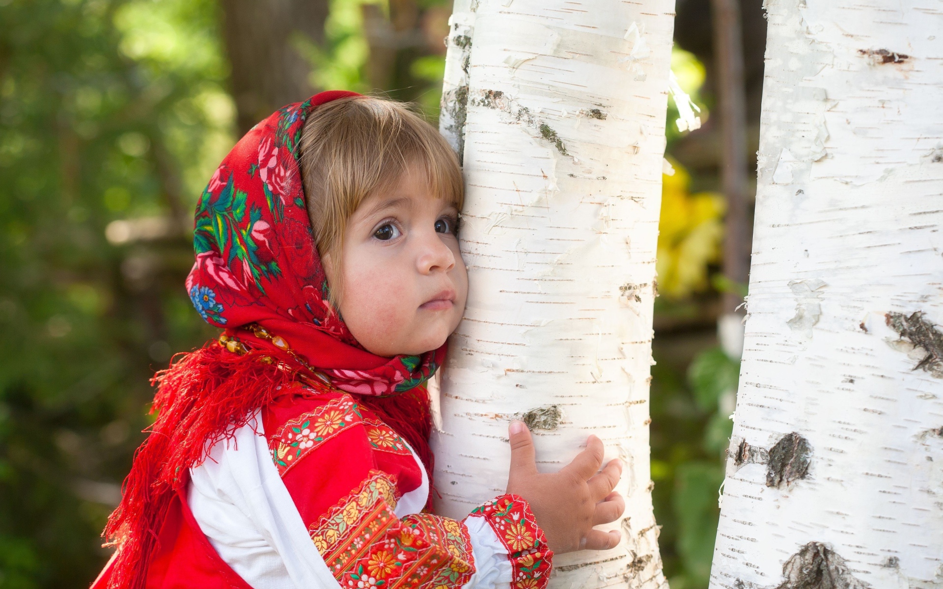 Маленькая девочка в красном платке обнимает березу