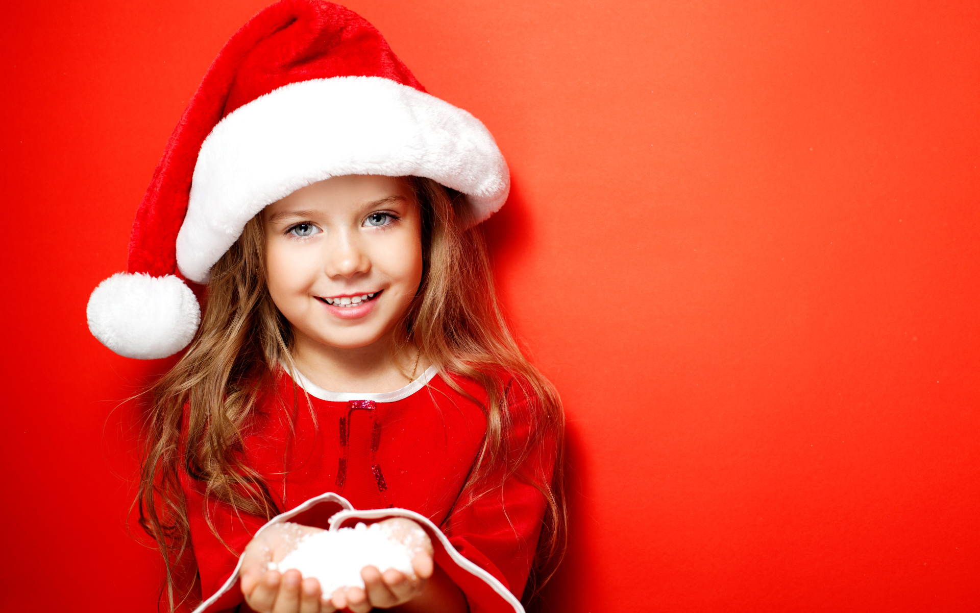 Маленькая девочка в новогодней шапке на красном фоне