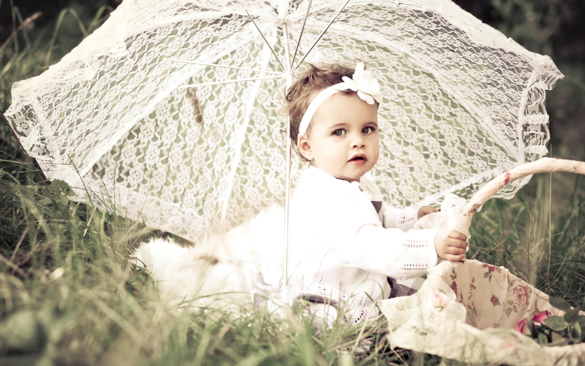 Маленькая девочка сидит на траве с большим белым зонтом