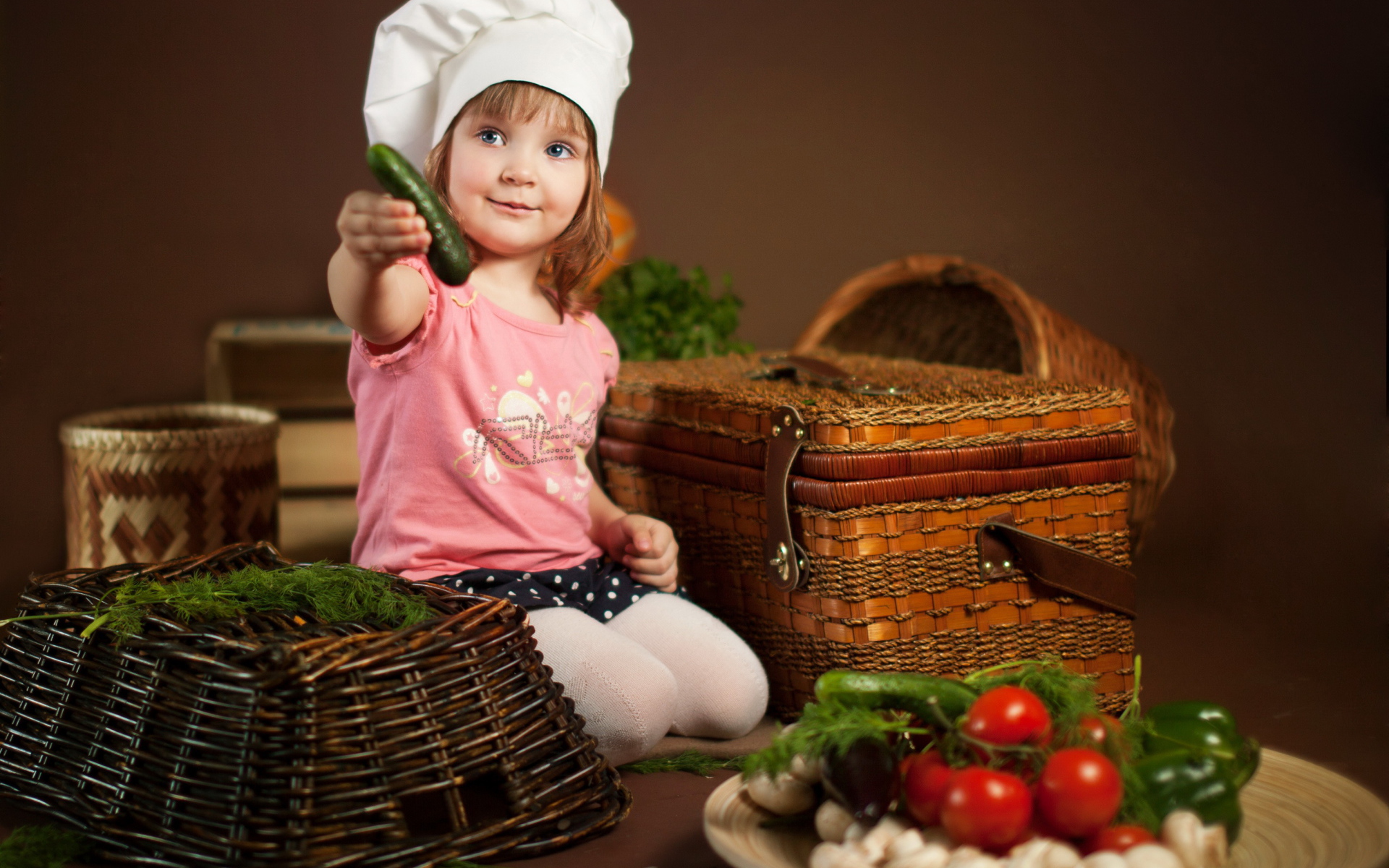 Маленькая девочка сидит на столе с корзинами и овощами