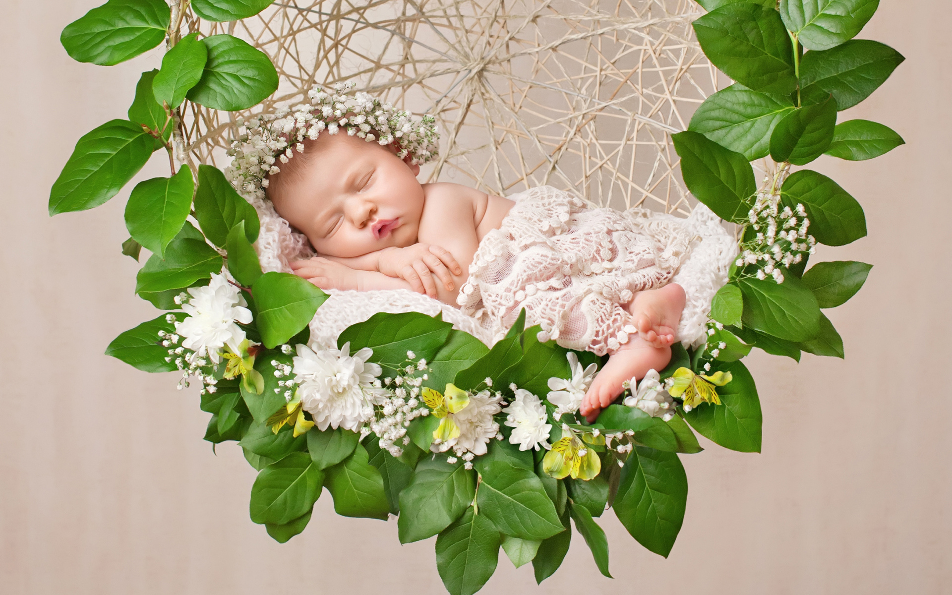 Маленькая девочка спит в колыбеле украшенной зелеными листьями