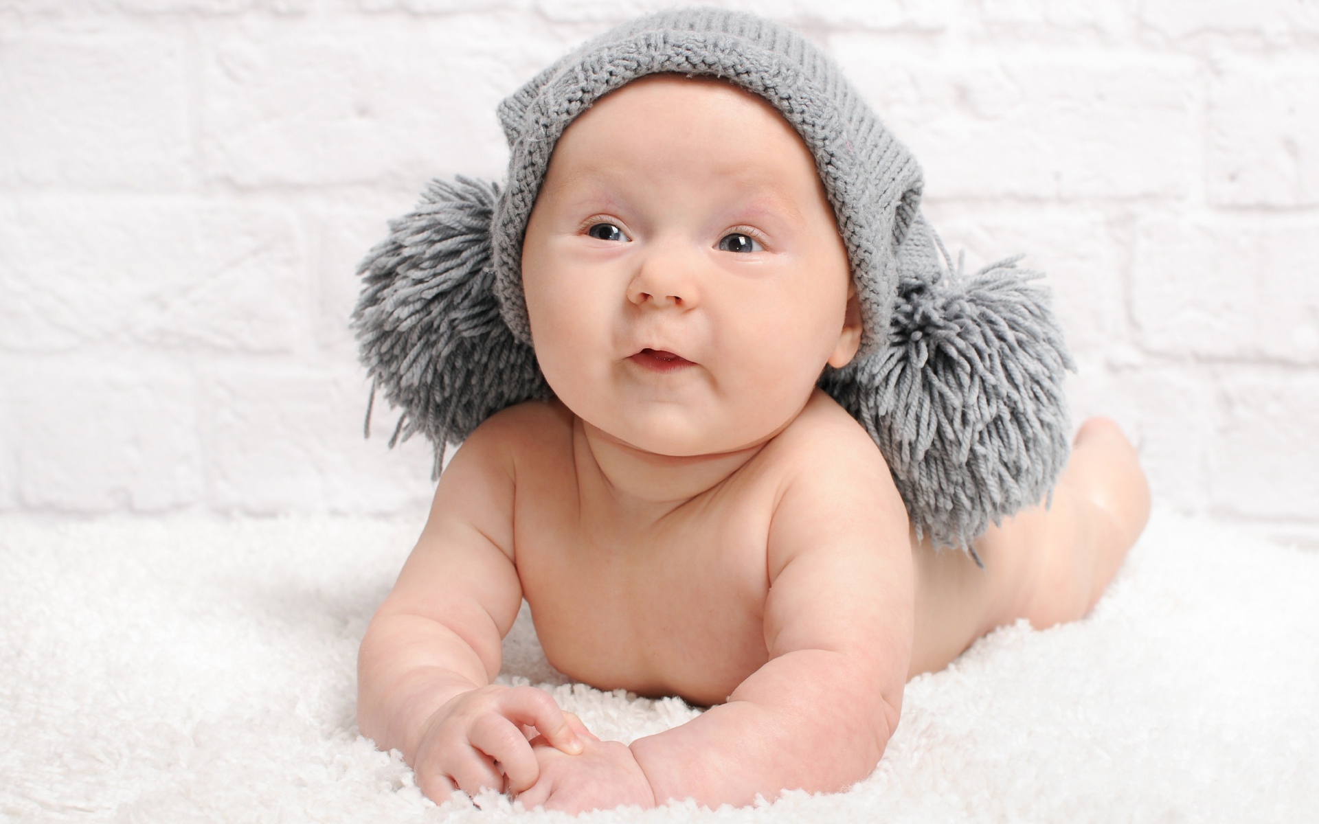 Улыбающийся грудной ребенок в серой шапке с бубонами