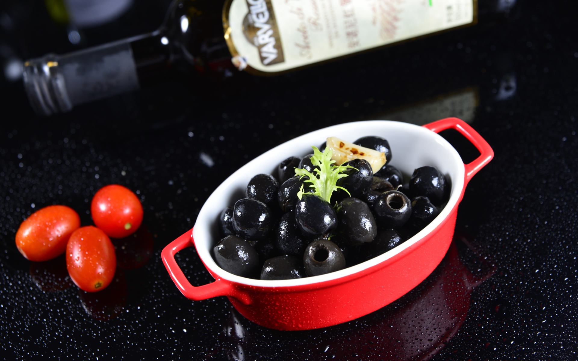 Черные оливки на столе с бутылкой и помидорами