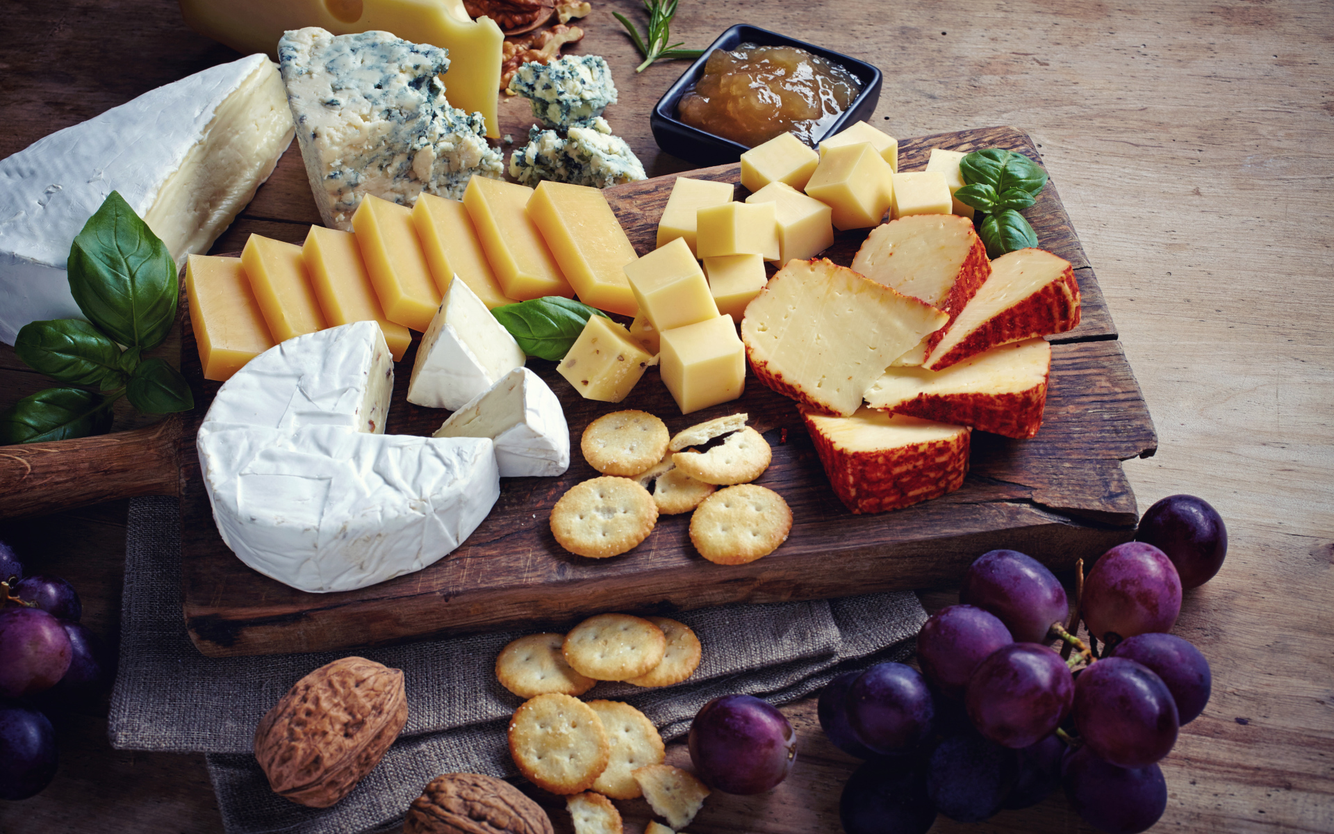 Сырная нарезка на разделочной доске на столе с виноградом и крекерами