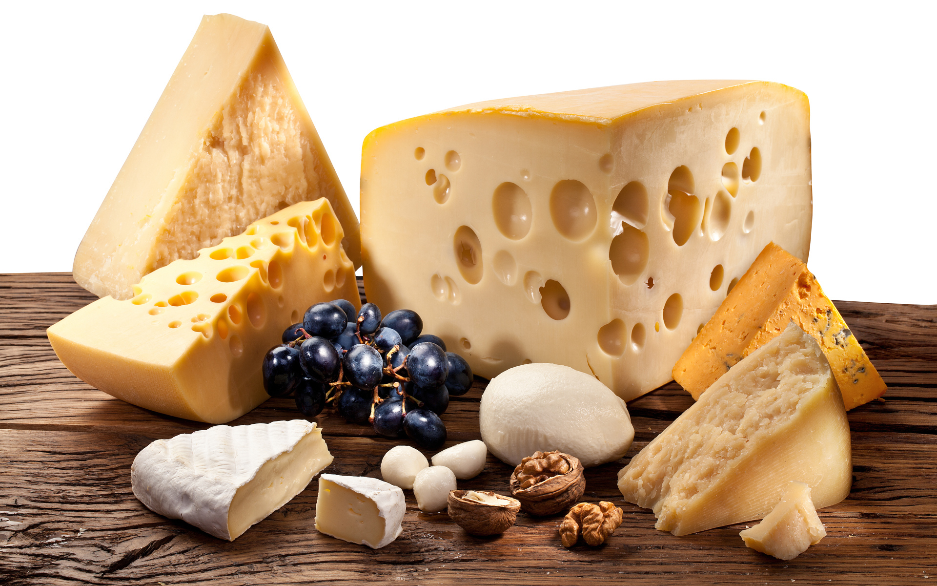 Куски сыра на деревянном столе с виноградом и грецким орехом