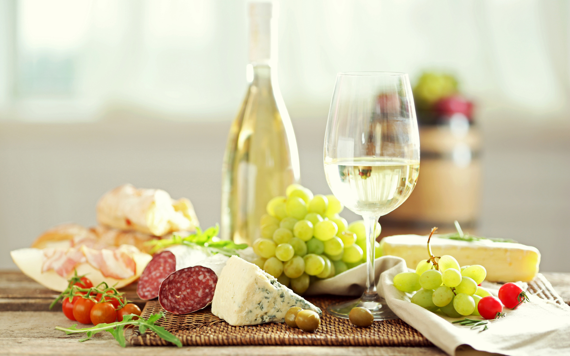 Белое вино на столе с сыром, колбасой и виноградом