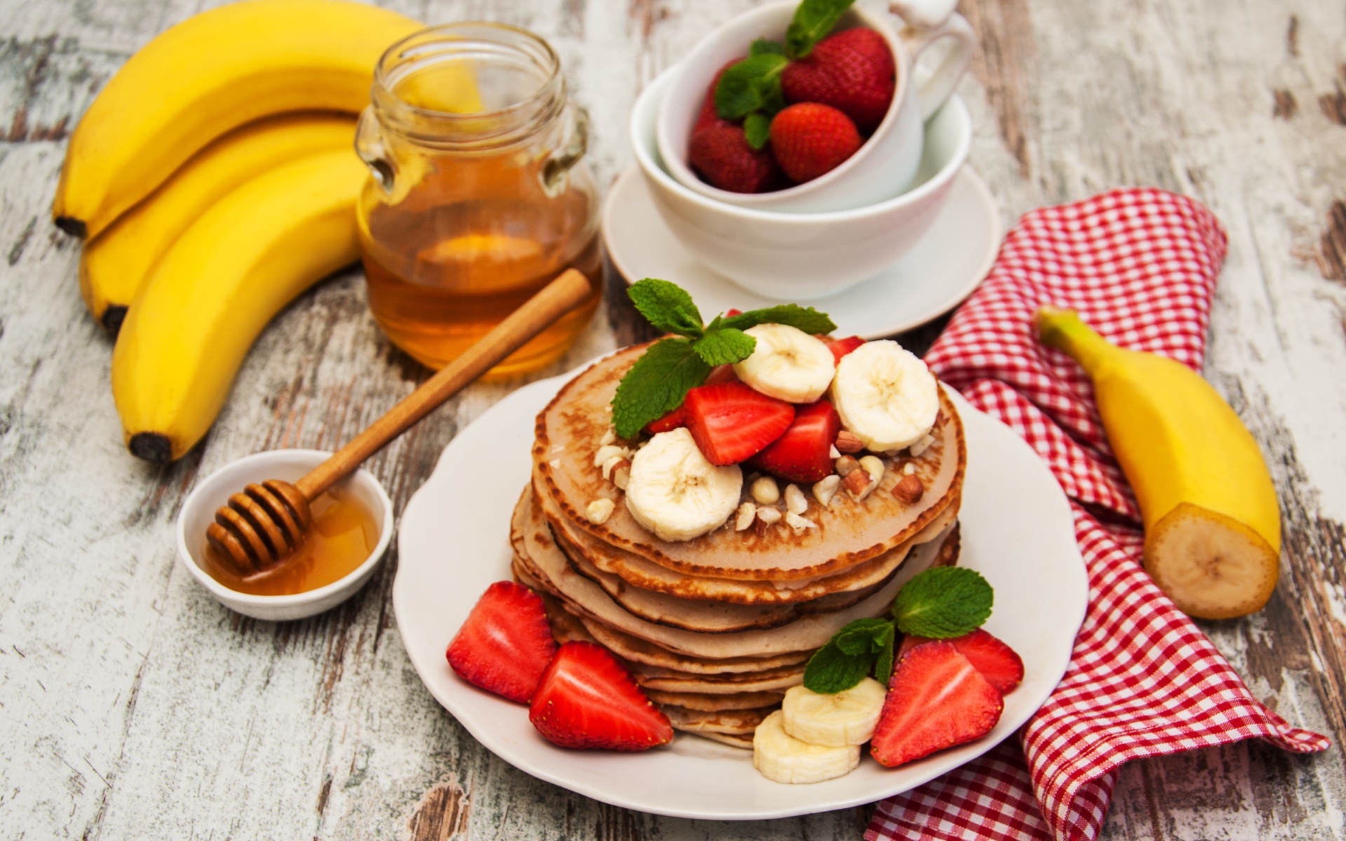 Оладьи с бананами и клубникой на столе с медом