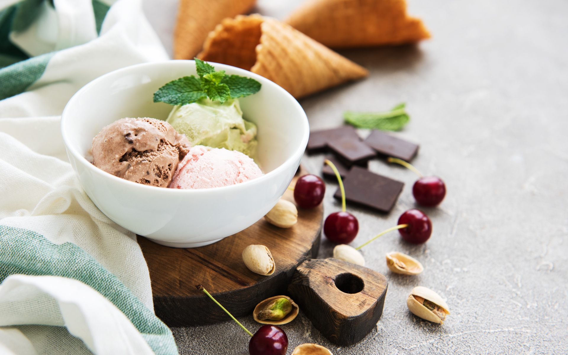 Шарики мороженого на столе вафельными рожками, черешней и фисташками