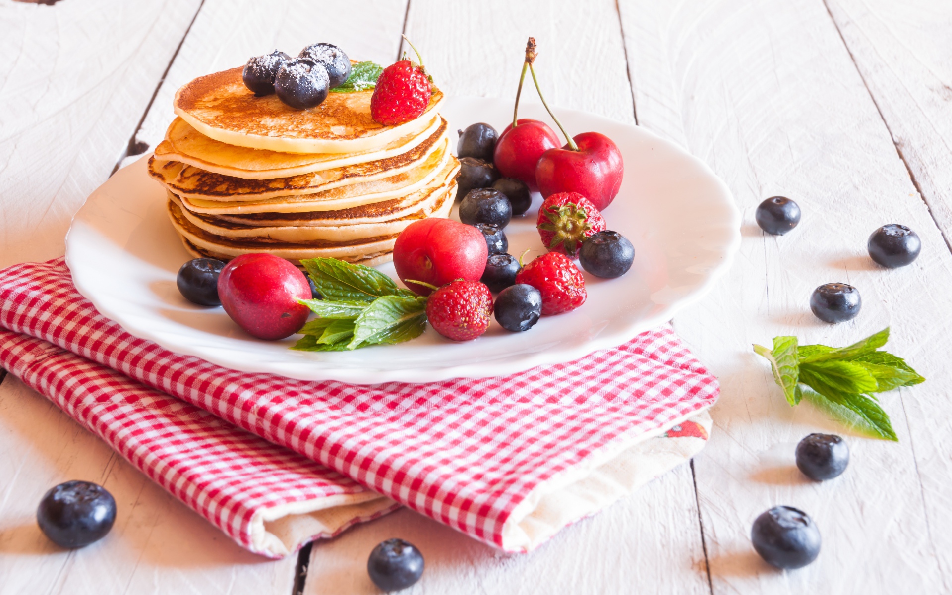 Оладья на белой тарелке с ягодами черники, черешни и клубники