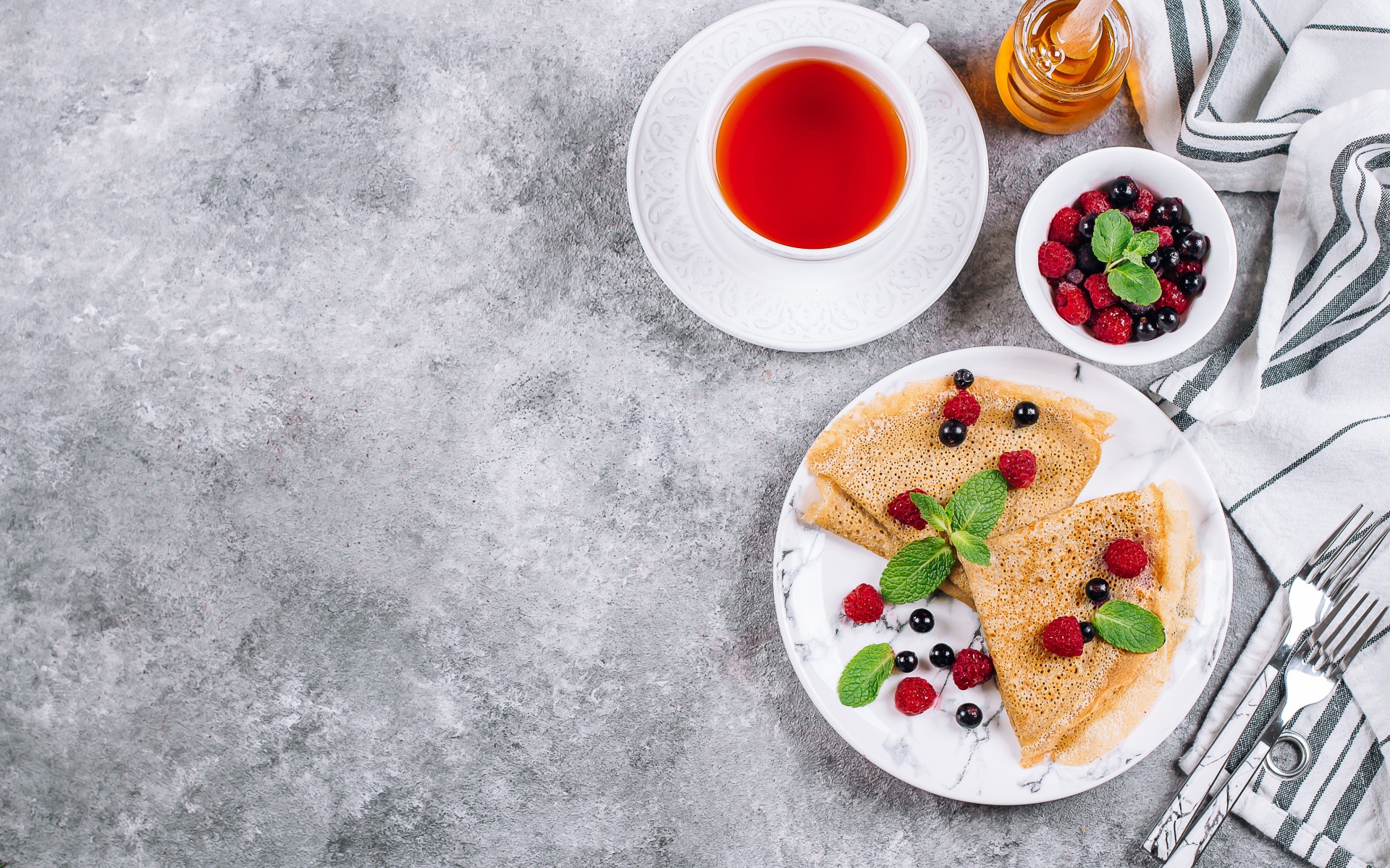Тонкие блинчики на столе с ягодами, чаем и медом