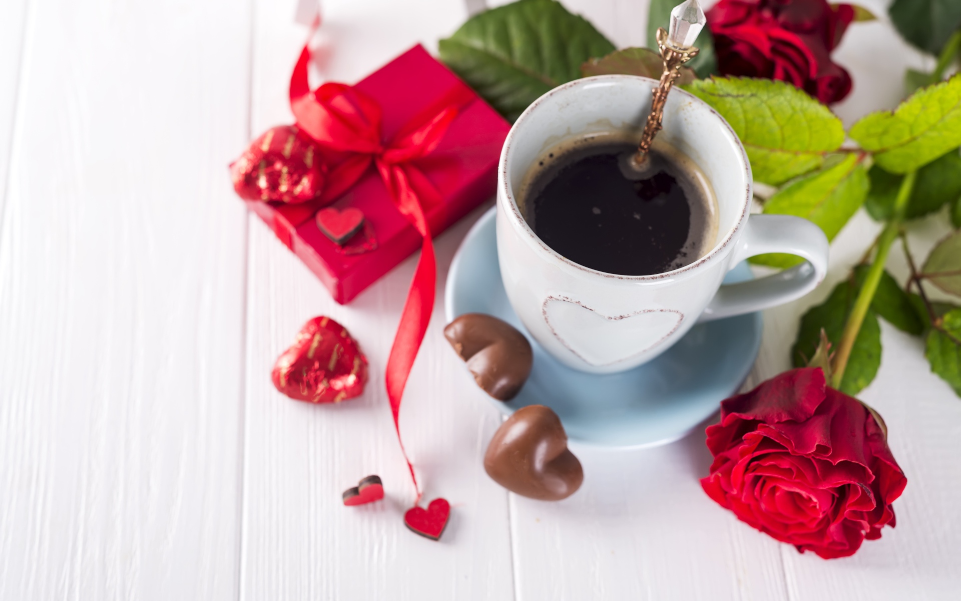 Чашка кофе на столе с шоколадными конфетами, подарком и красной розой