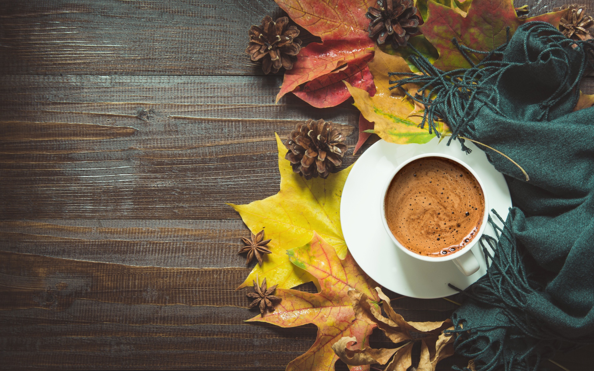 Чашка кофе на столе с шарфом, желтыми листьями и шишками