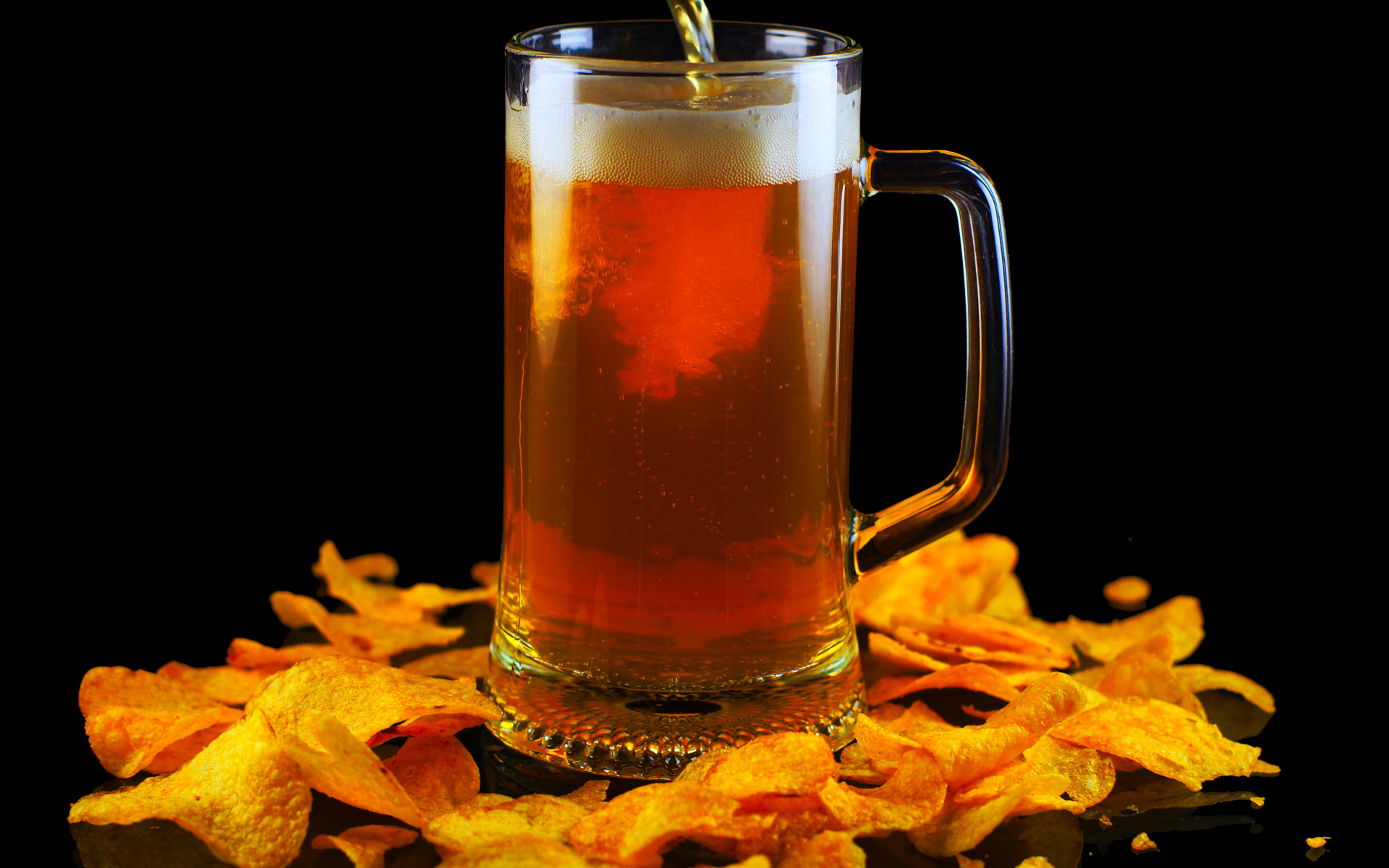 Бокал пива с чипсами на черном фоне