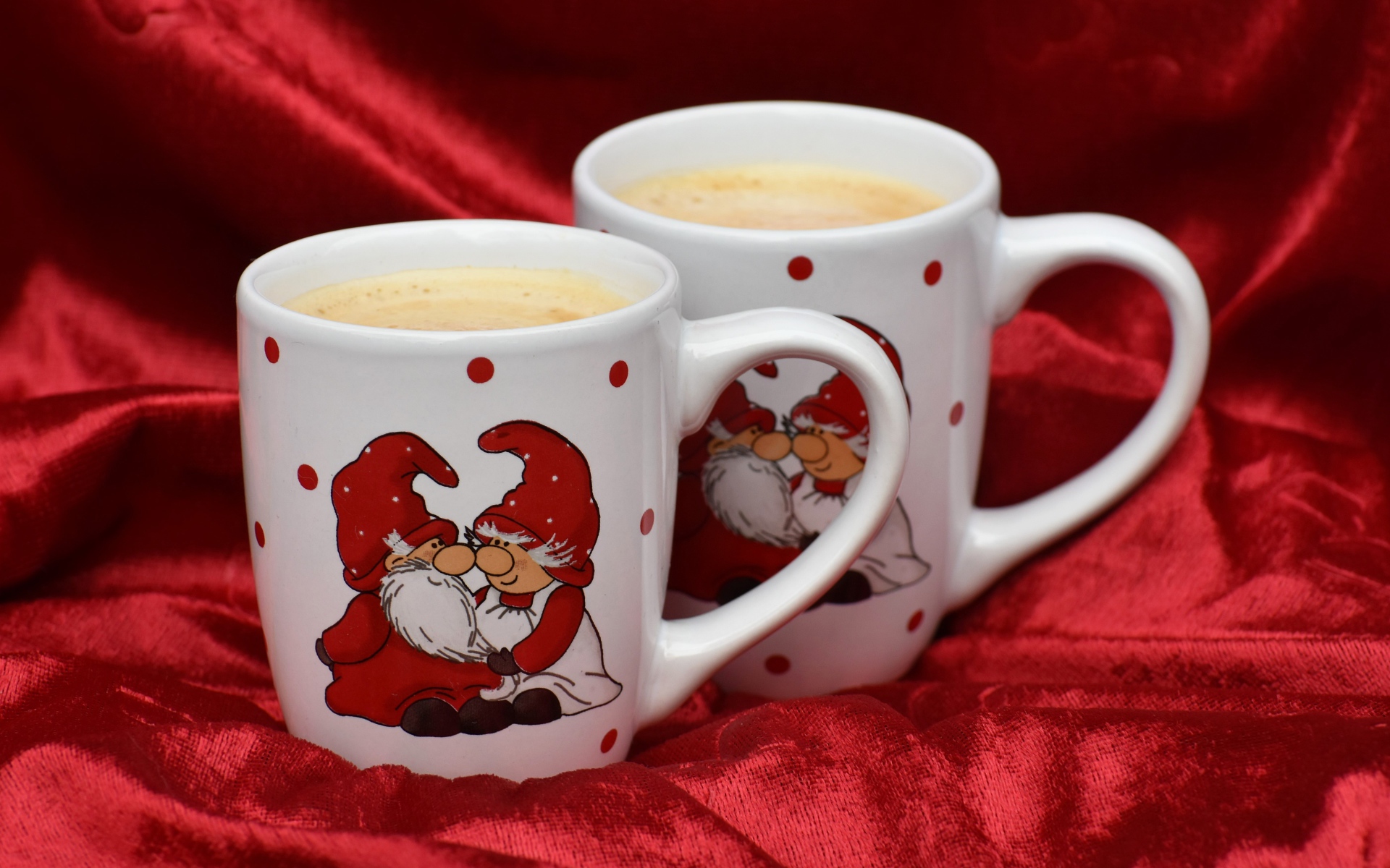 Две белые чашки кофе с рисунком стоят на красной ткани