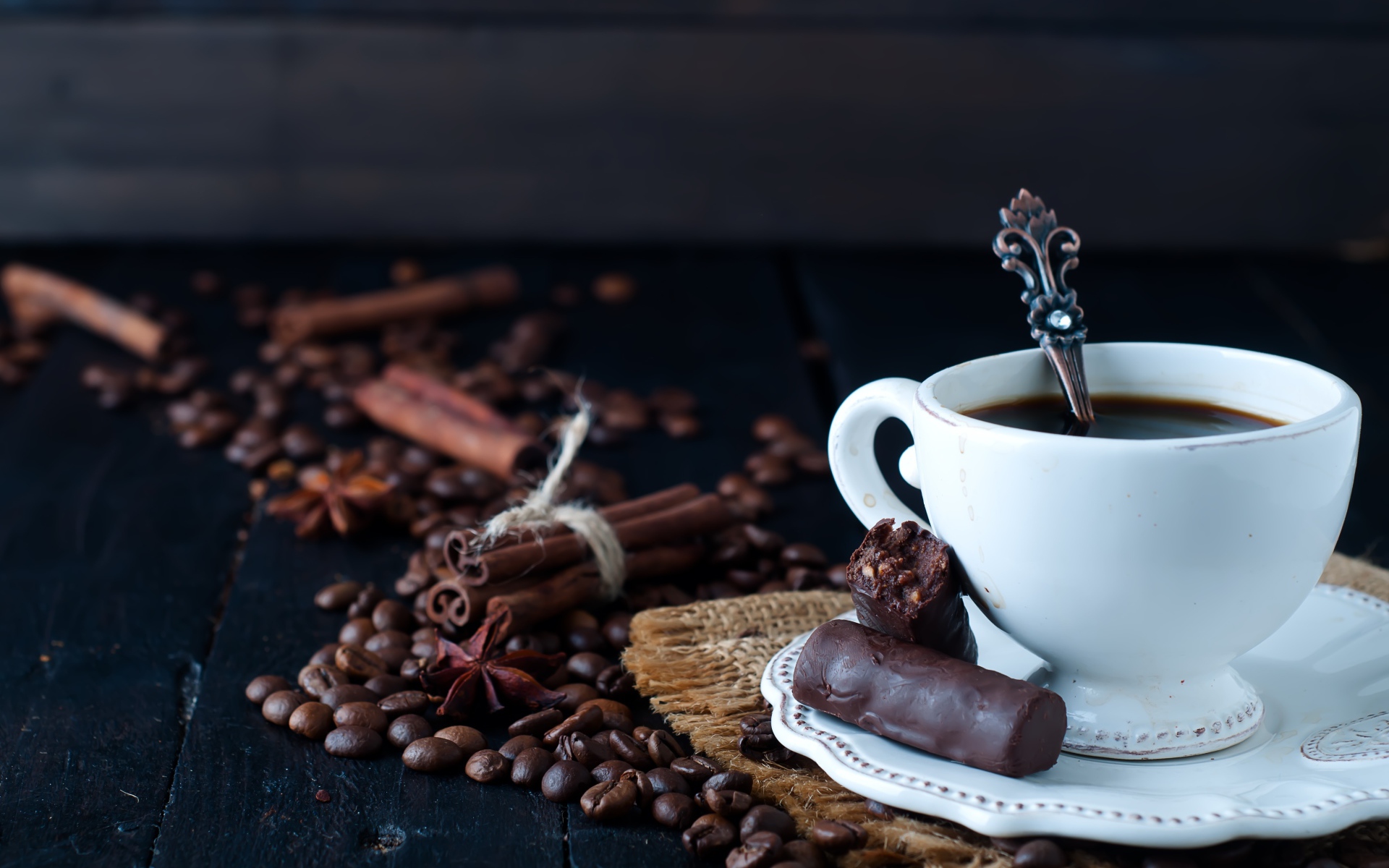 Белая чашка кофе на столе с конфетами, корицей, бадьяном и зернами
