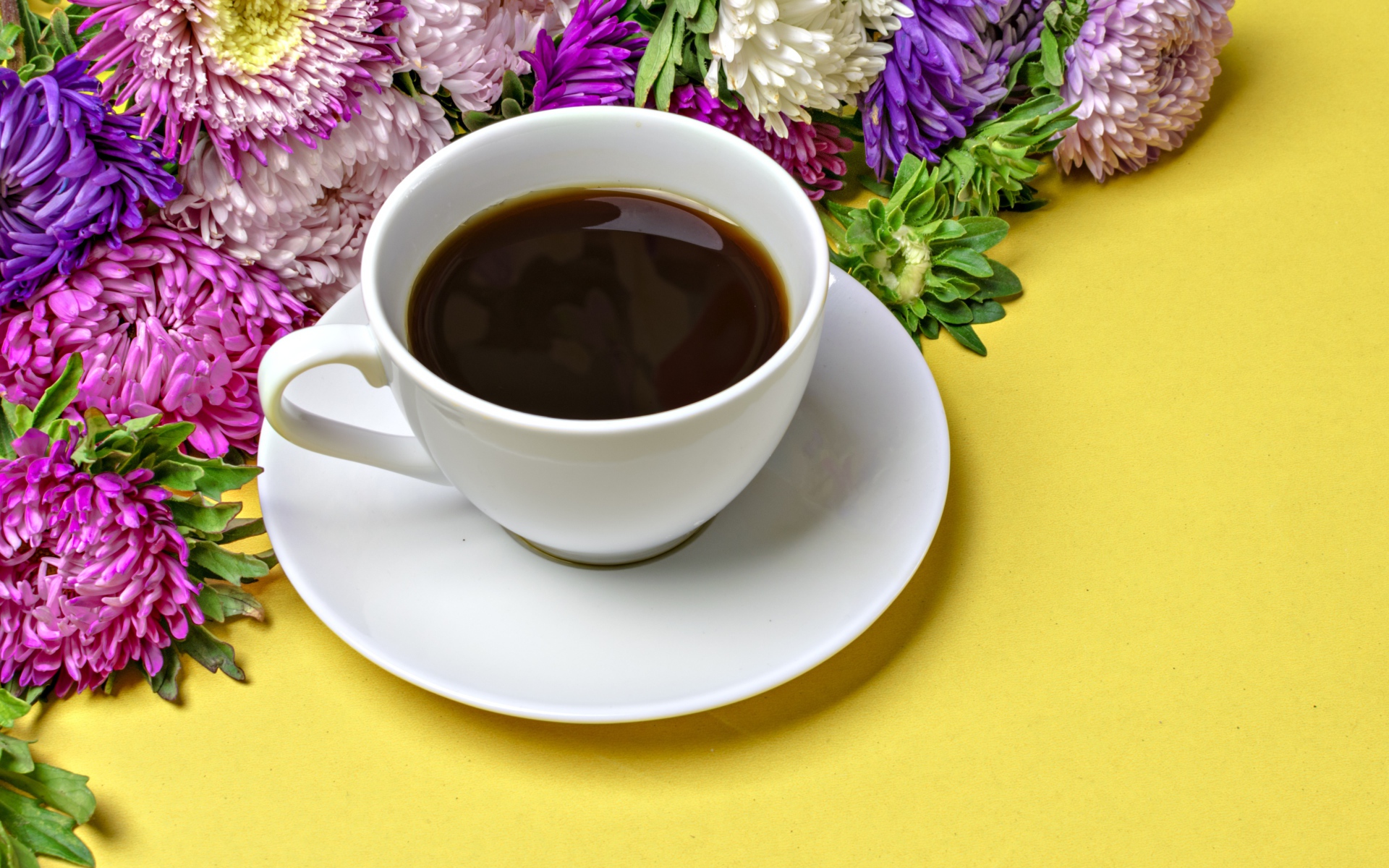 Белая чашка кофе на желтом фоне с букетом цветов астры