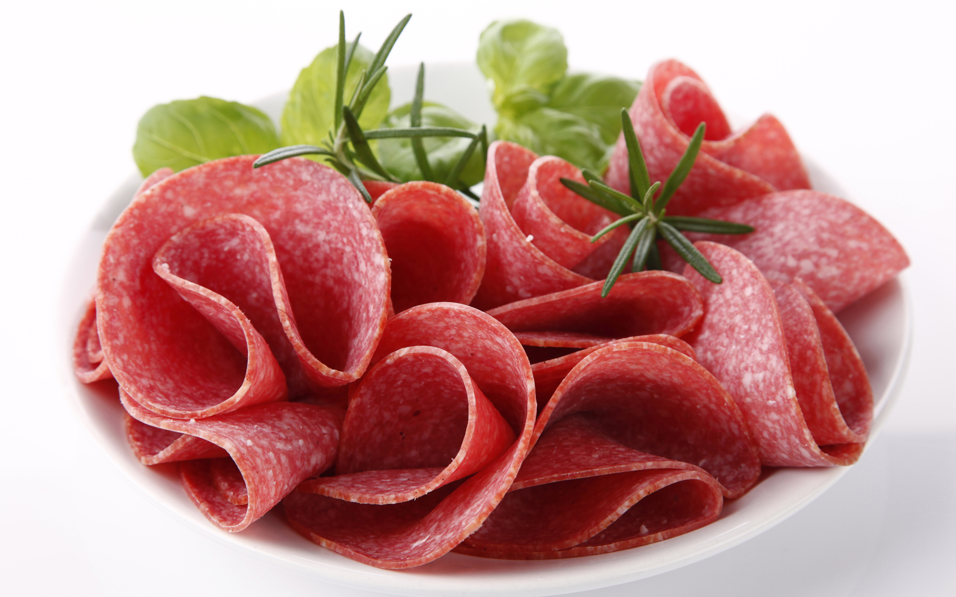 Тонкие кусочки колбасы на тарелке с зеленью 