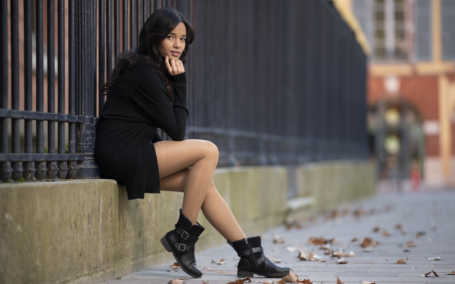 Молодая девушка в черном сидит у железного забора