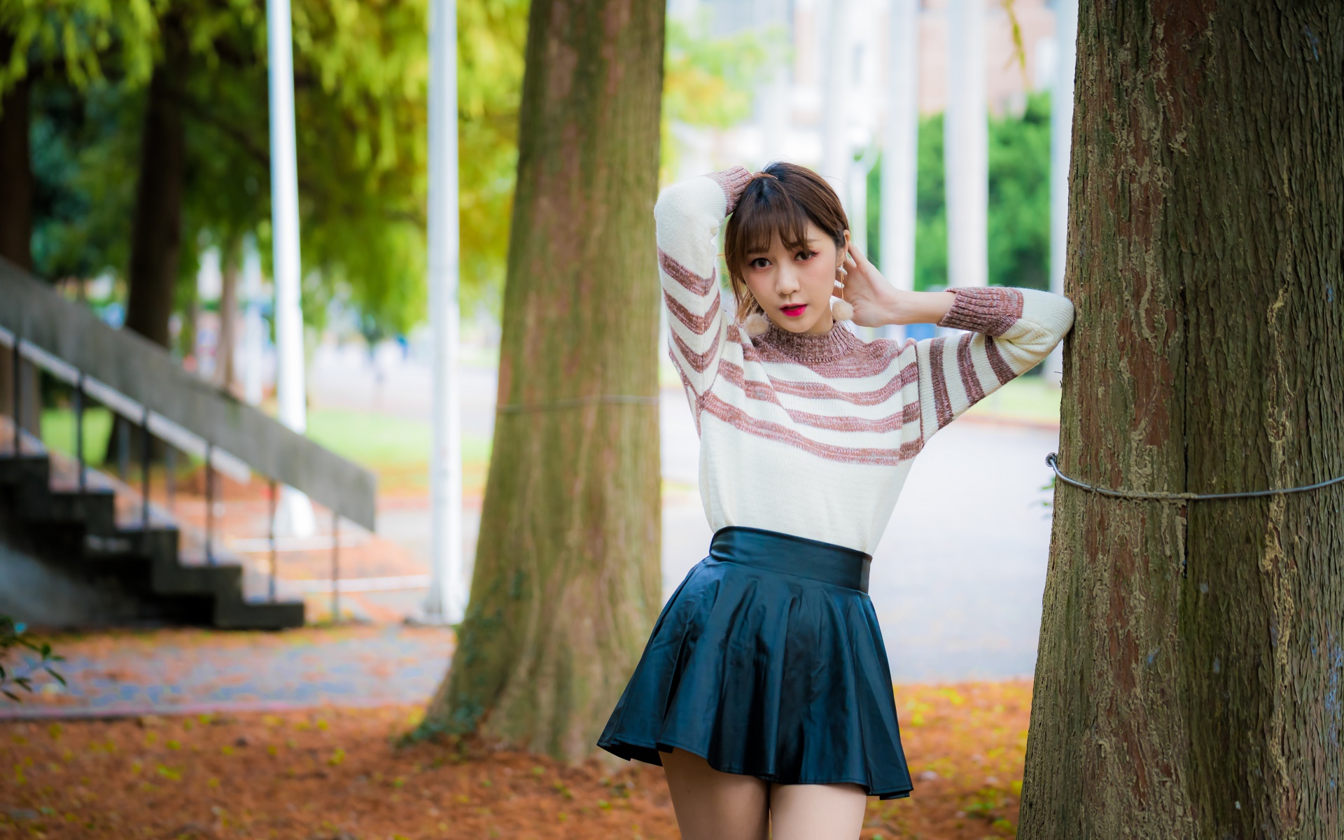 Девушка азиатка стоит в короткой юбке у дерева