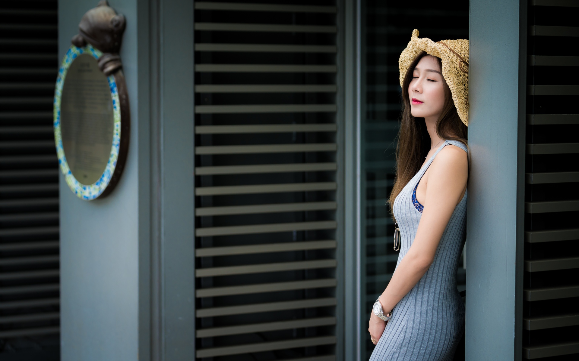 Девушка азиатка с закрытыми глазами стоит у стены 