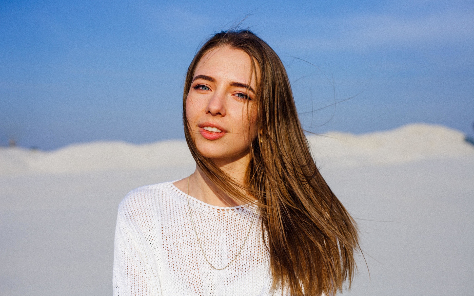 Красивая голубоглазая девушка в белом свитере на фоне голубого неба