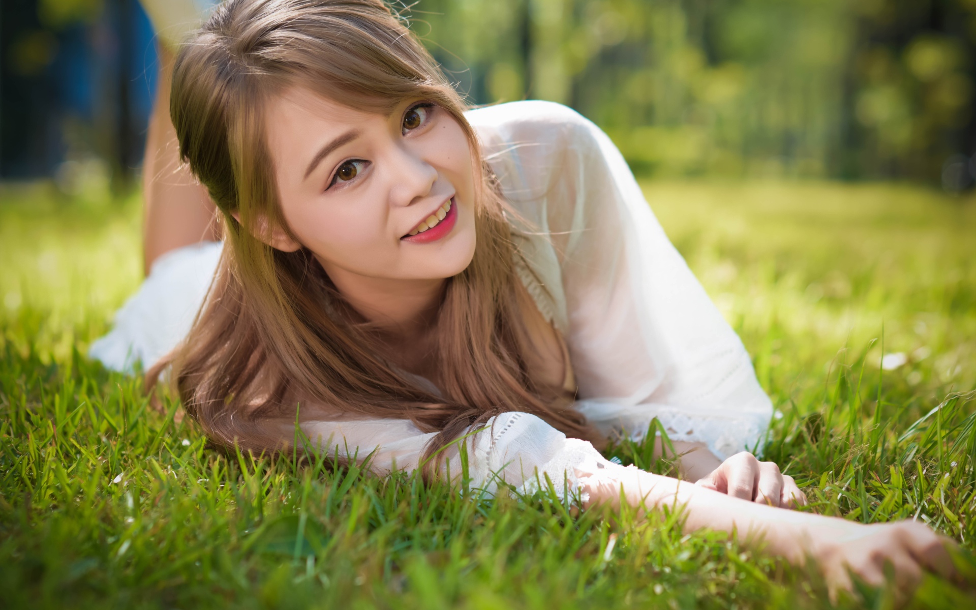 Красивая кареглазая девушка азиатка лежит на зеленой траве
