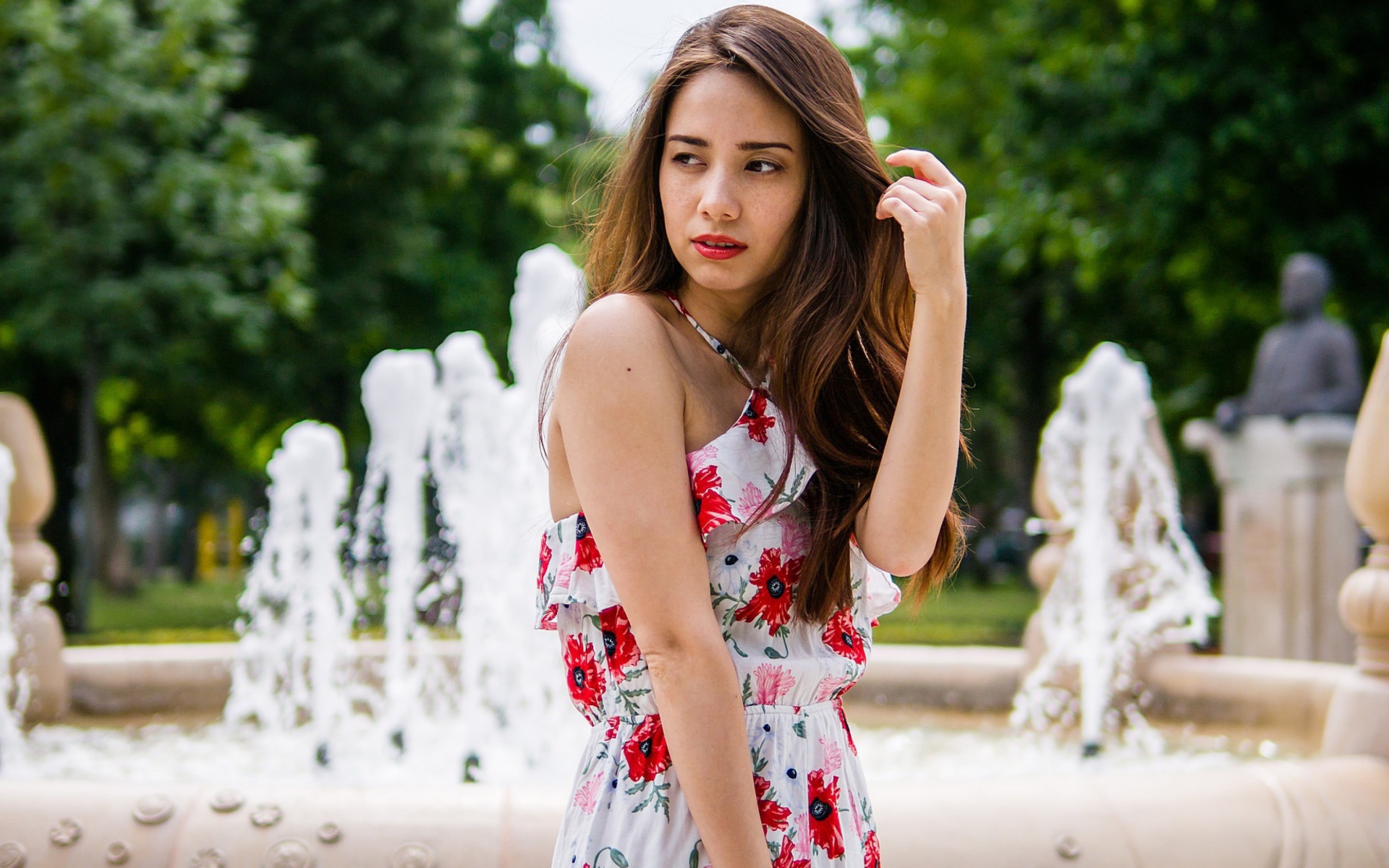 Красивая шатенка в цветастом платье у фонтана летом