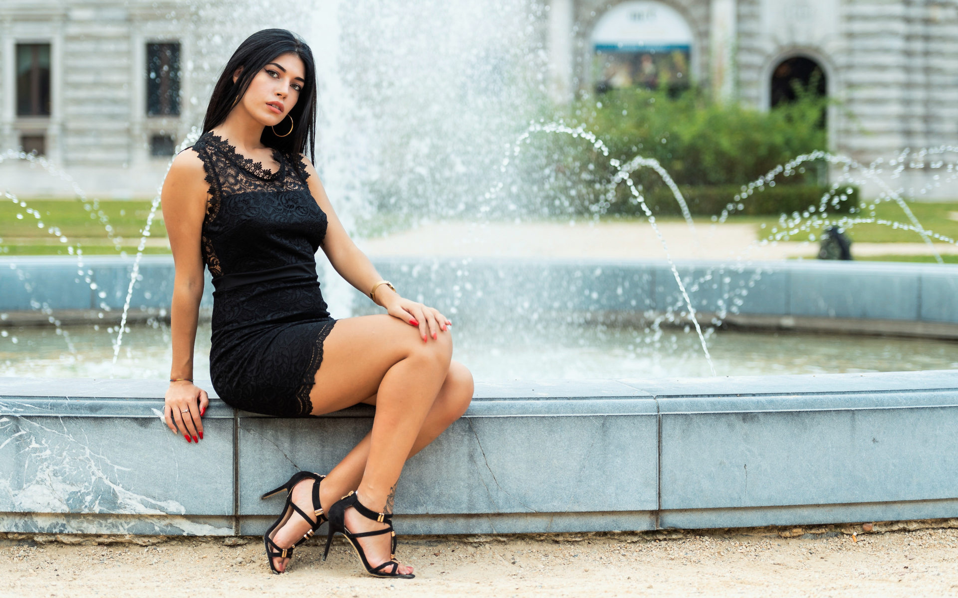 Красивая брюнетка в черном платье сидит у фонтана