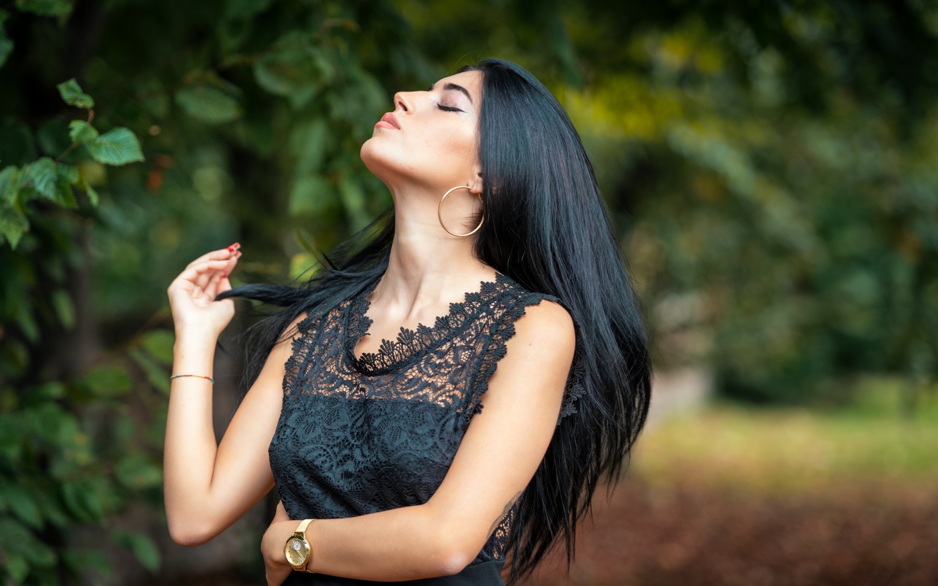 Красивая брюнетка в черном платье с закрытыми глазами в парке