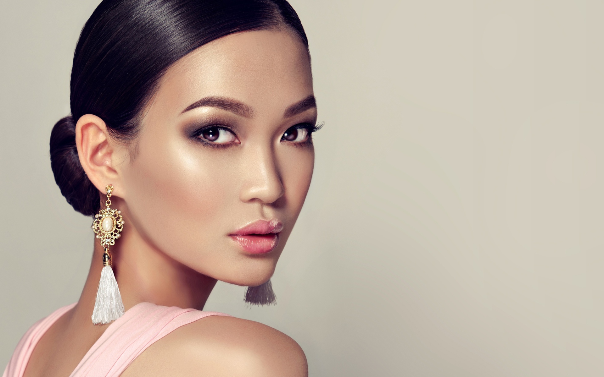 Красивая девушка с прической и сережками в ушах на сером фоне