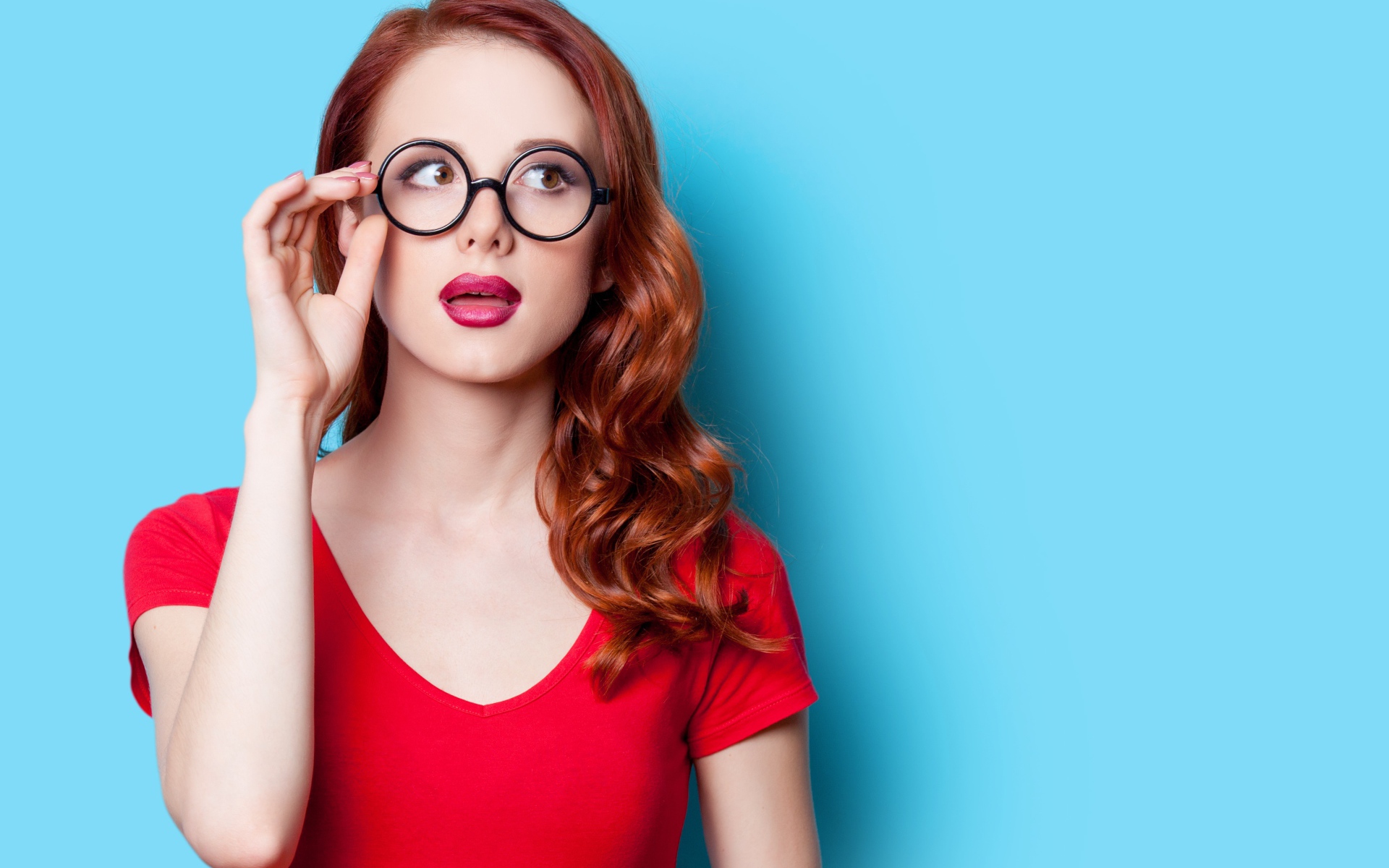 Красивая рыжеволосая девушка в очках на голубом фоне