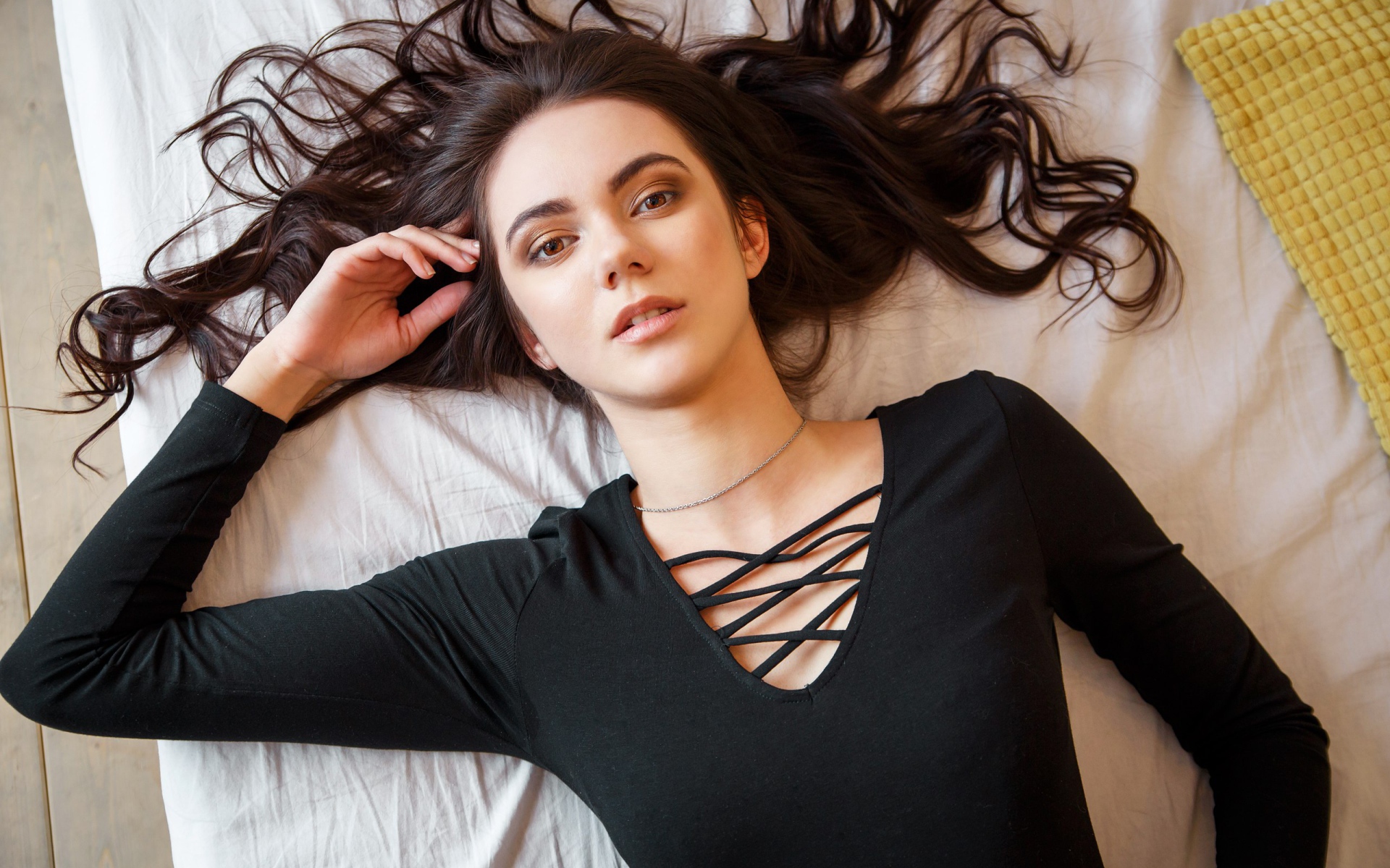 Кареглазая девушка в черном лежит на кровати