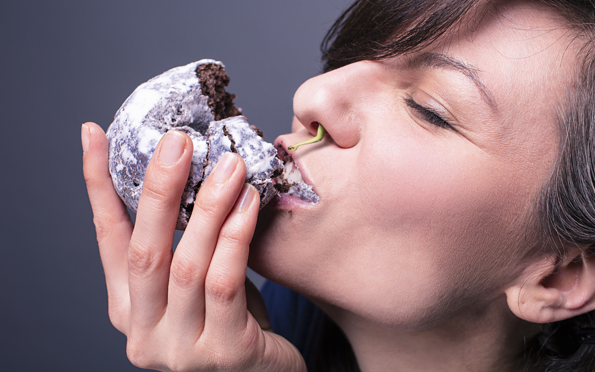 Девушка ест шоколадный пряник на сером фоне