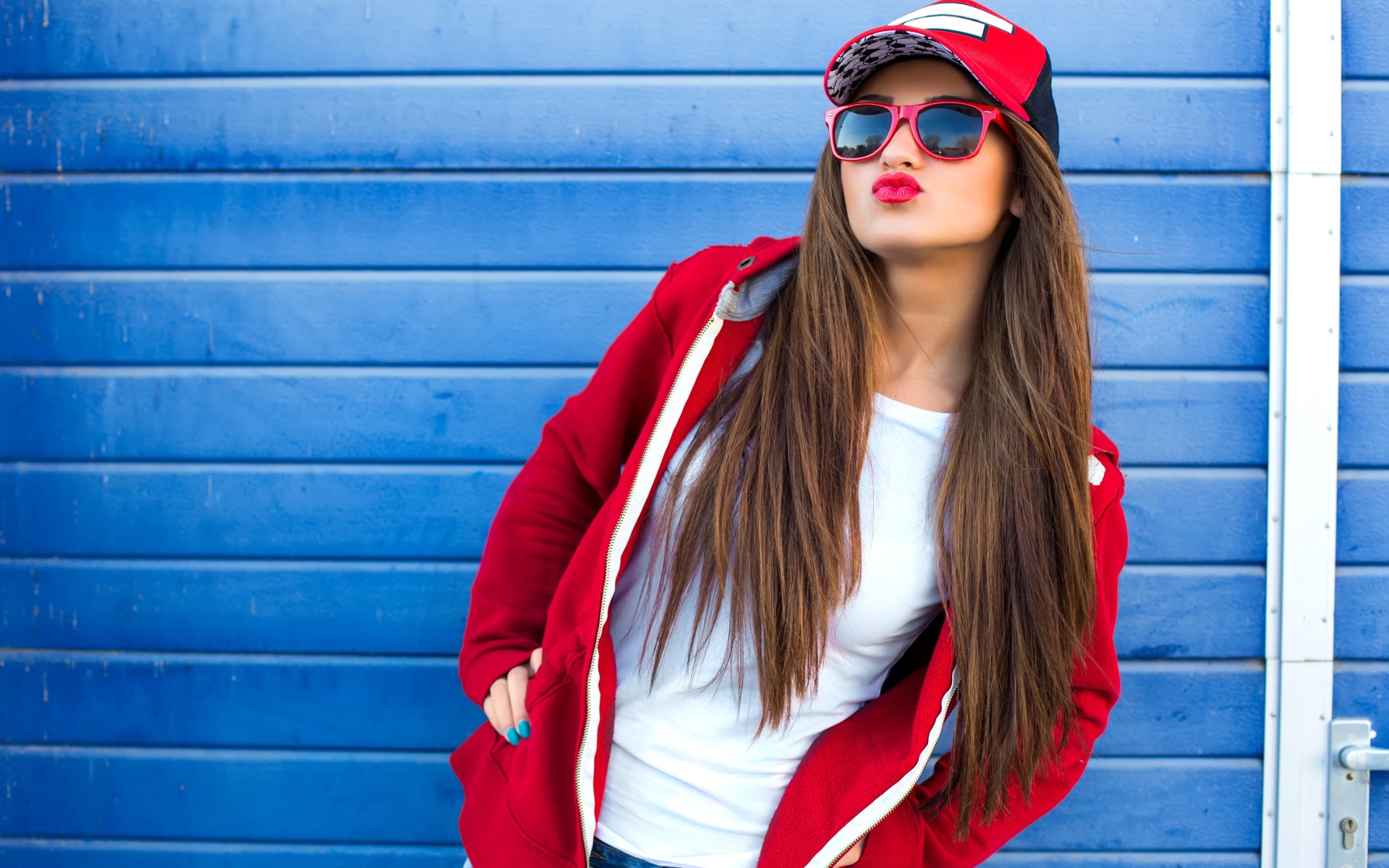 Девушка в бейсболке и солнечных очках у стены