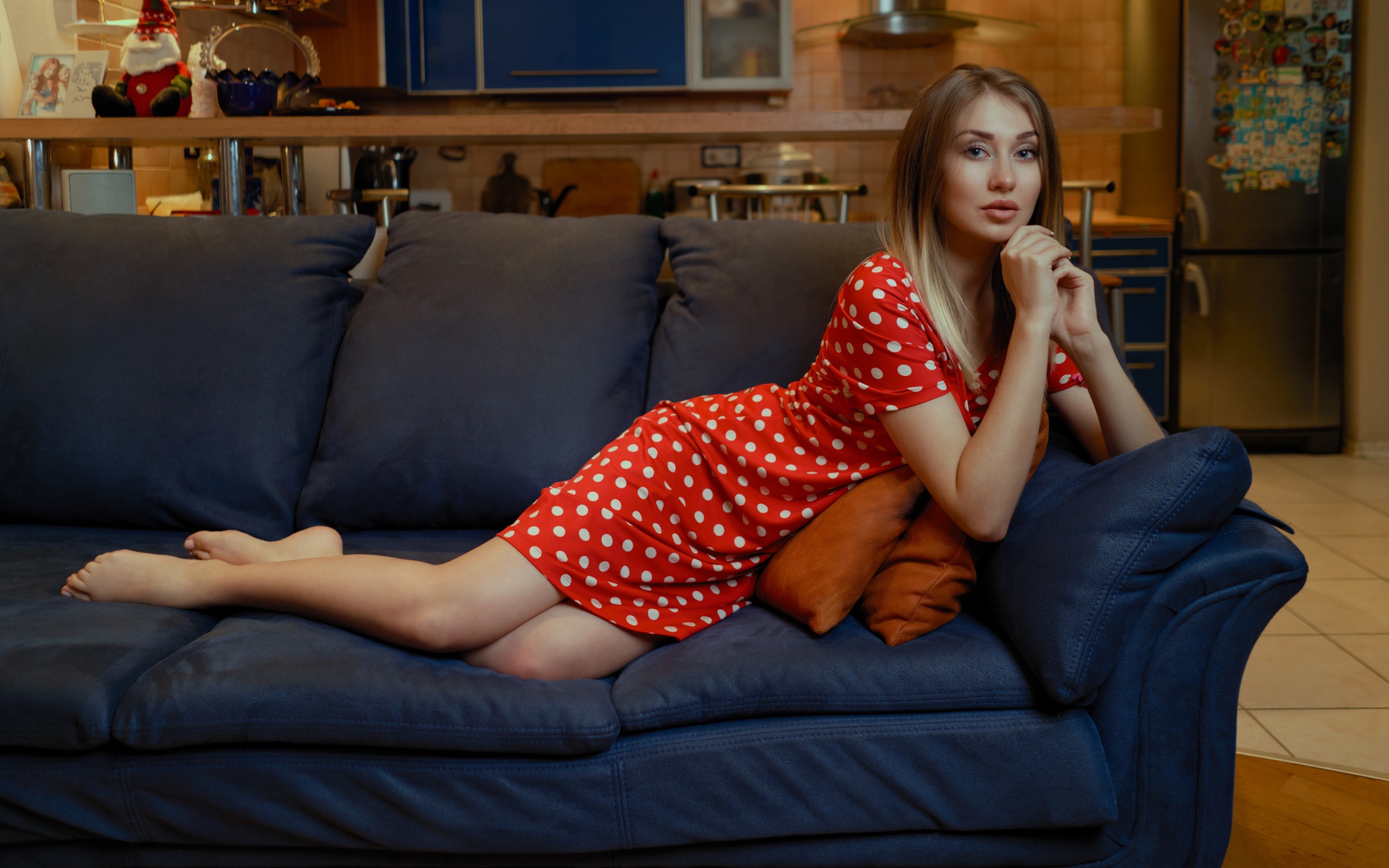 Девушка в красном платье в горошек лежит на диване