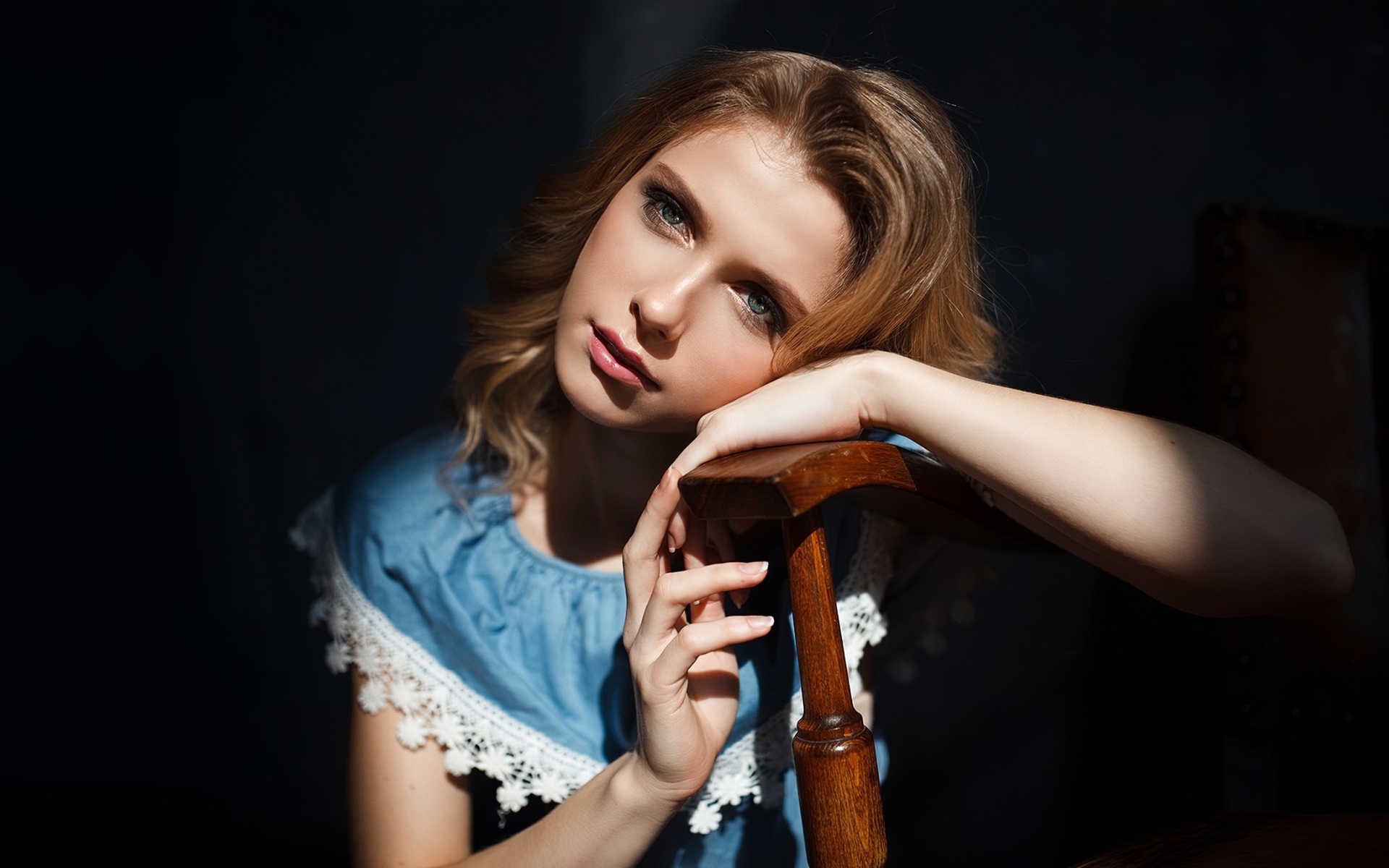 Грустная девушка сидит облокотившись об спинку кресла