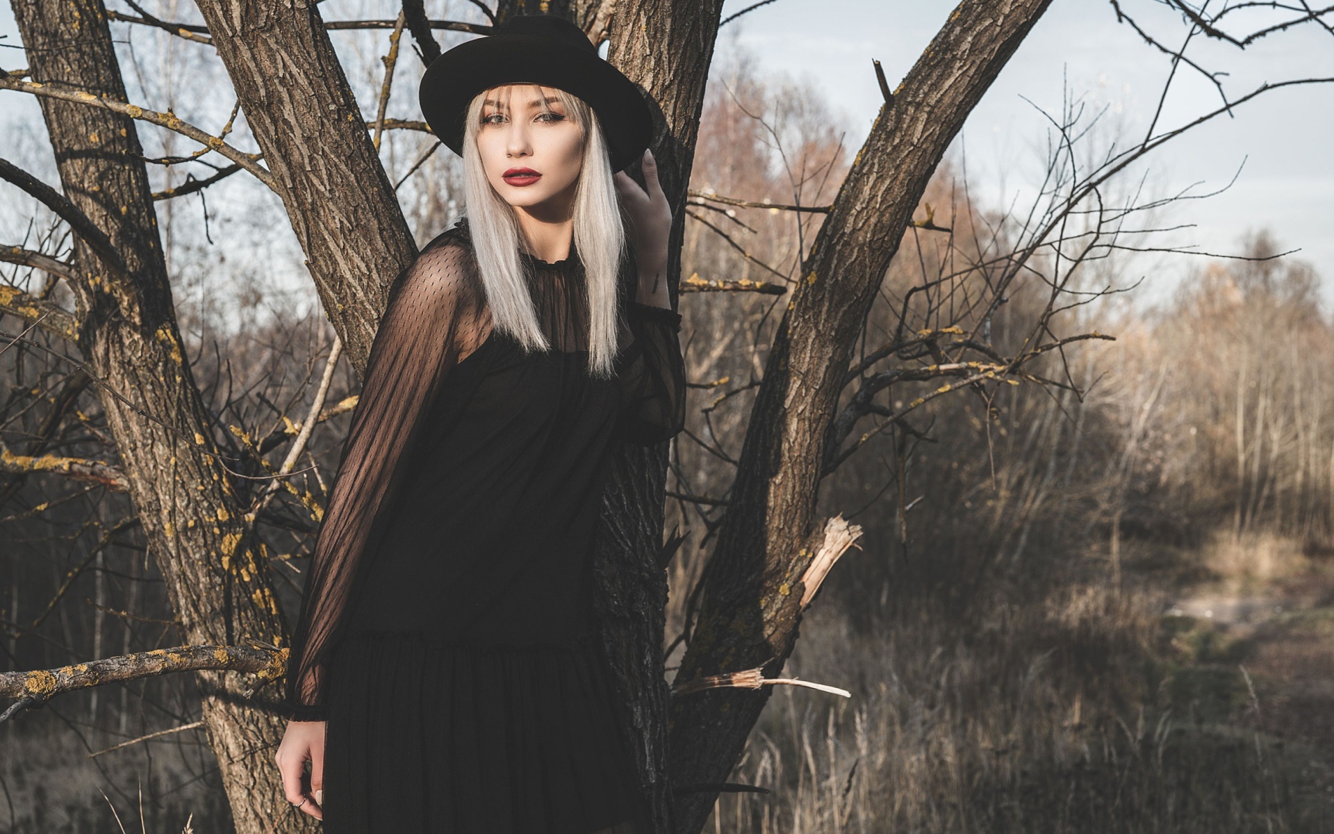 Молодая блондинка в черной шляпе у дерева