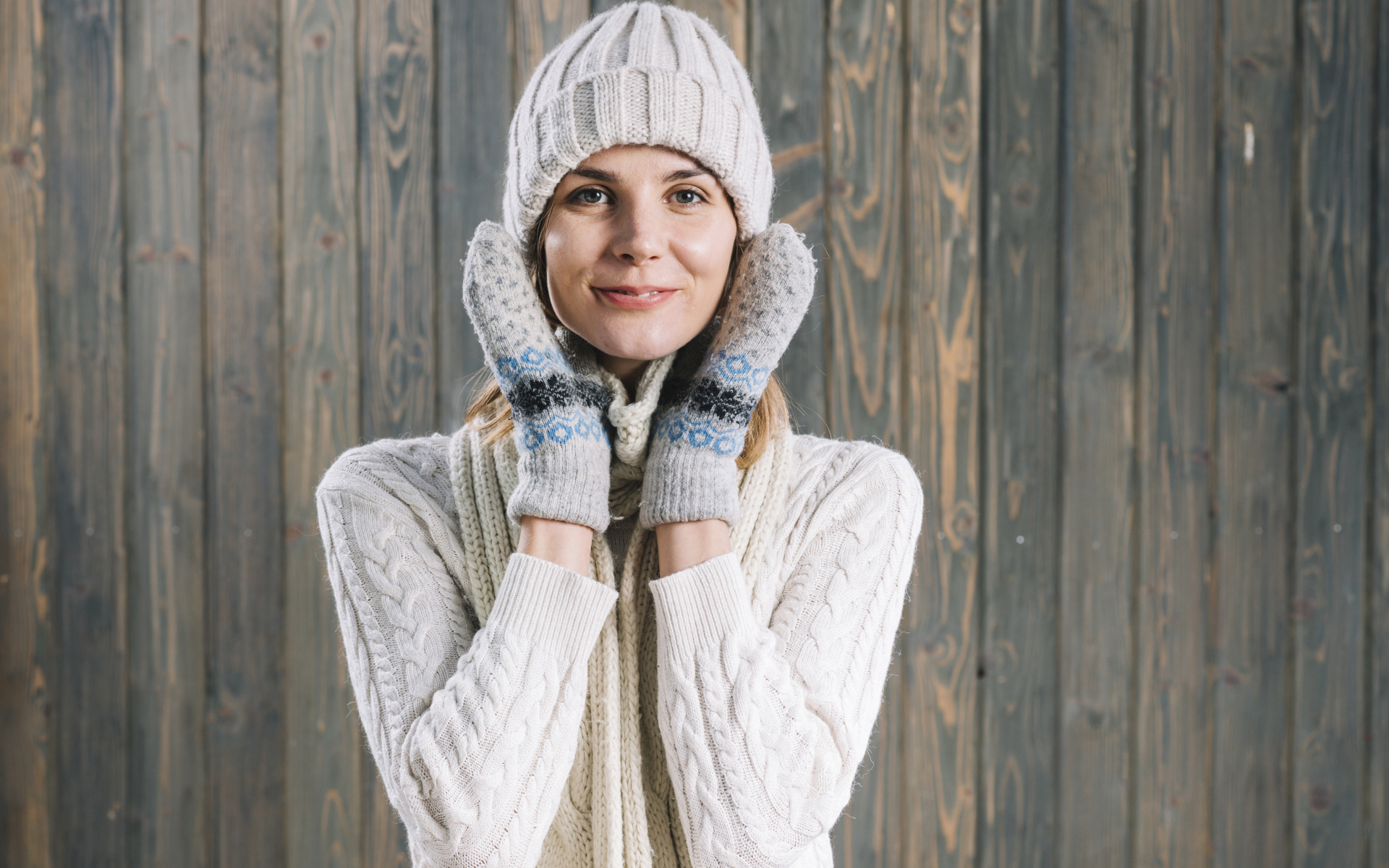 Молодая девушка на шапке, варежках  и теплой шапке на фоне забора