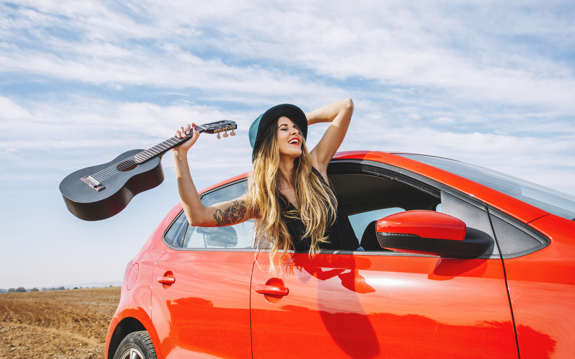 Молодая девушка с гитарой в красной машине летом