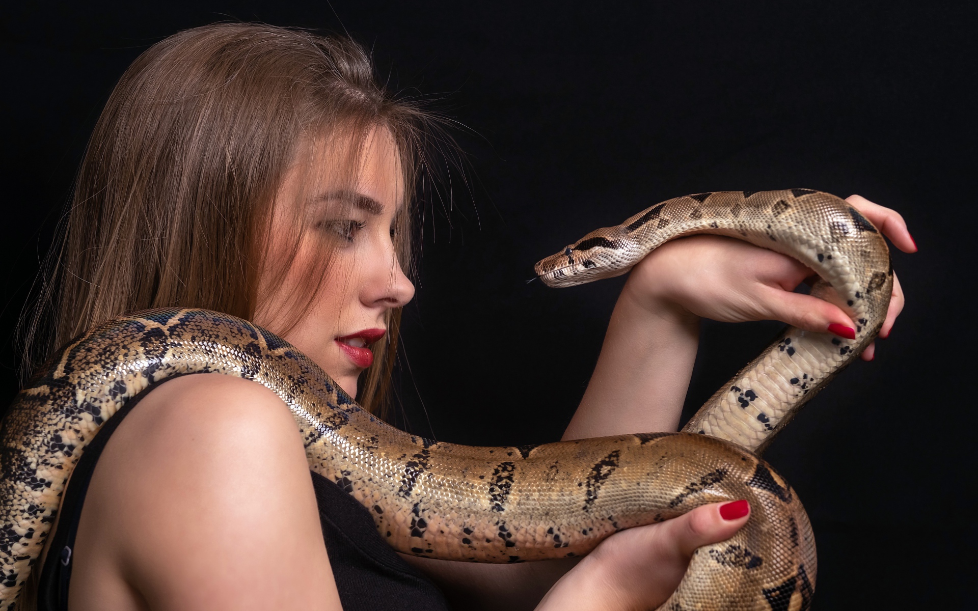 Молодая девушка со змеей в руках на черном фоне