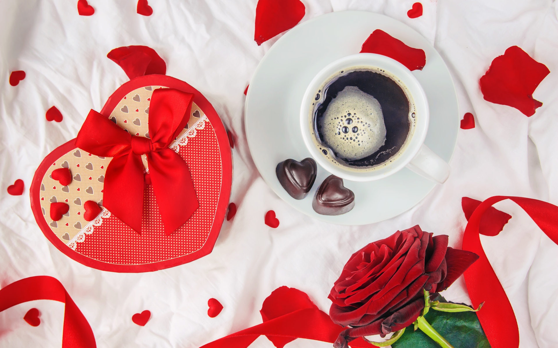 Кружка с кофе и шоколадными конфетами на столе с подарком и красной розой 