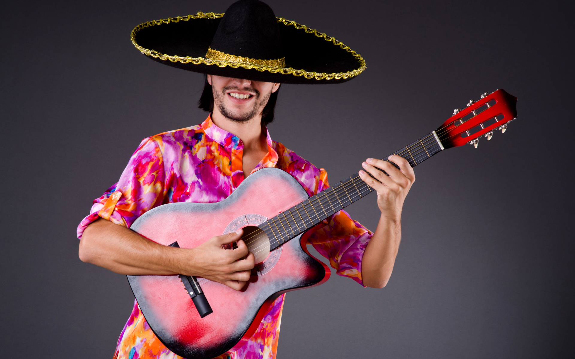 Мужчина в сомбреро с гитарой в руках на сером фоне