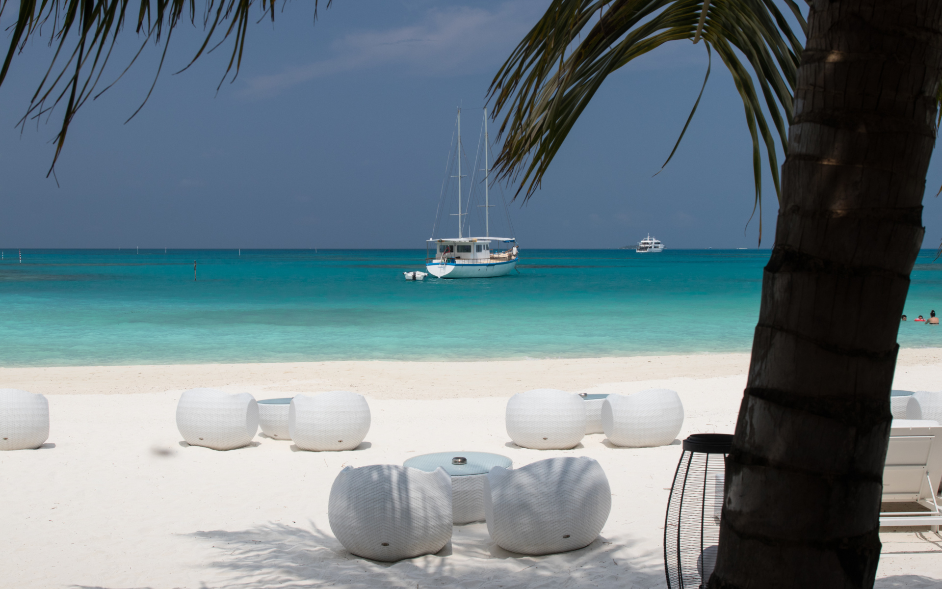 Белые кресла и столики на белом песке на пляже у голубой воды