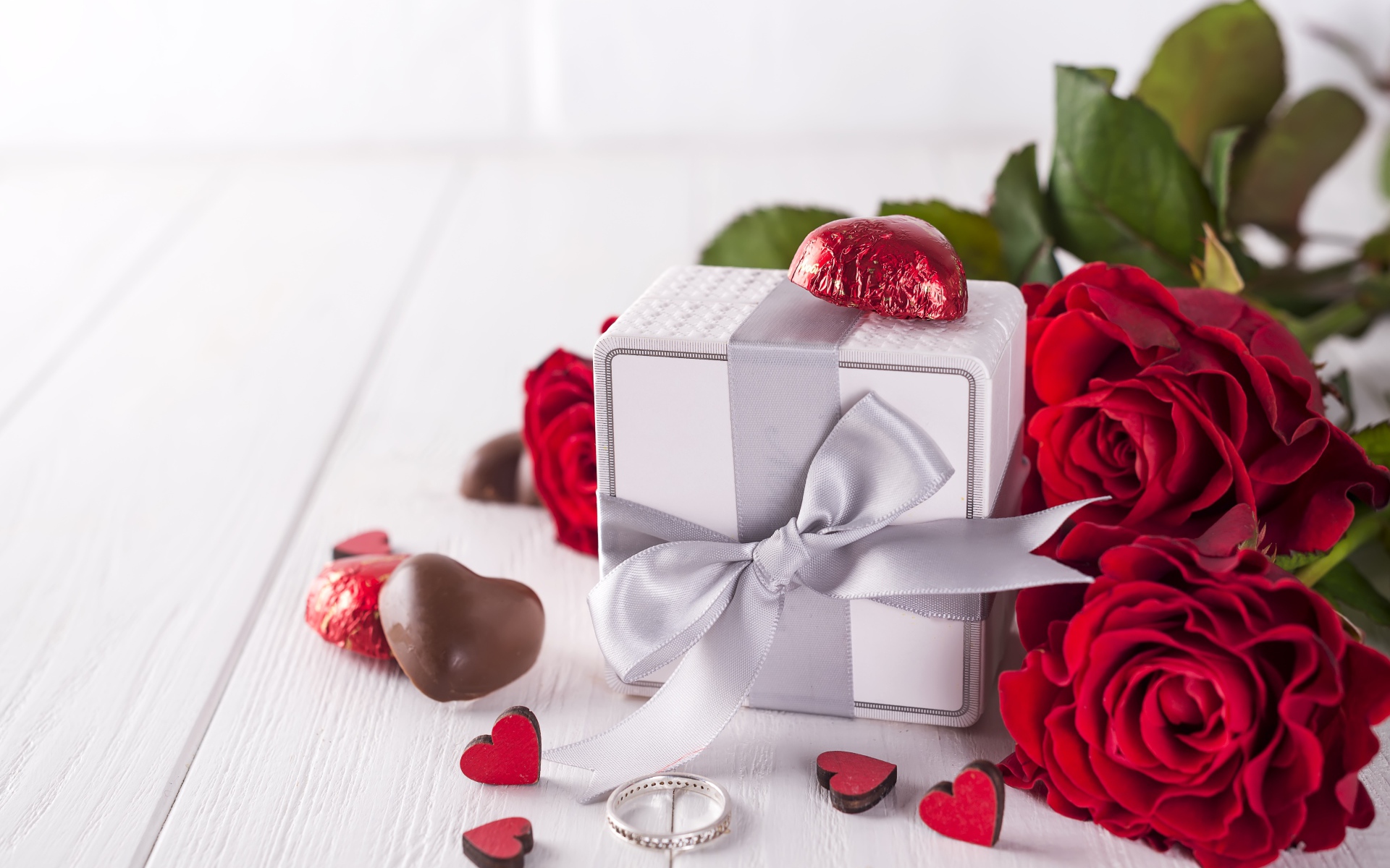 Подарок на столе с конфетами и букетом красных роз 
