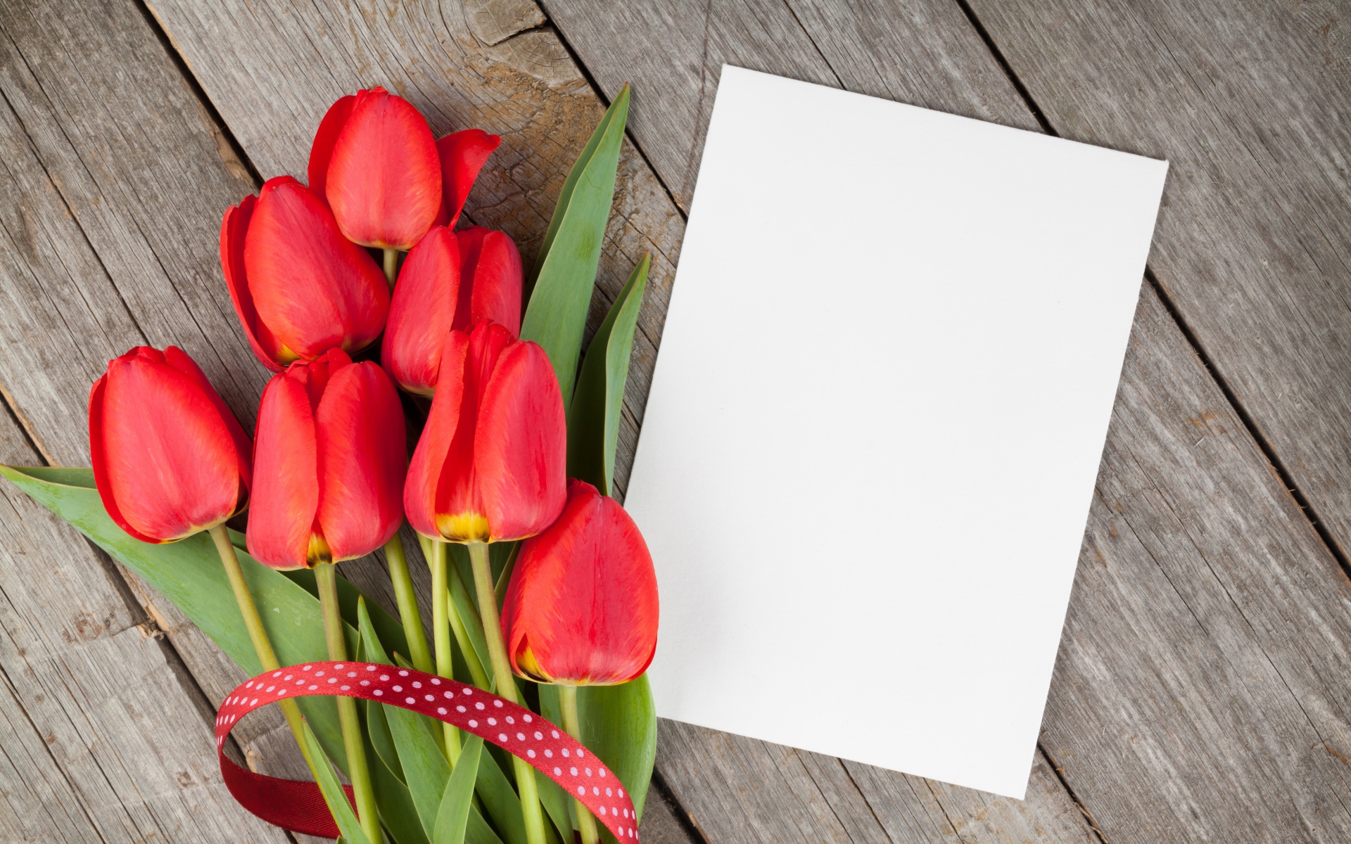 Букет красных тюльпанов с листом бумаги на деревянном столе