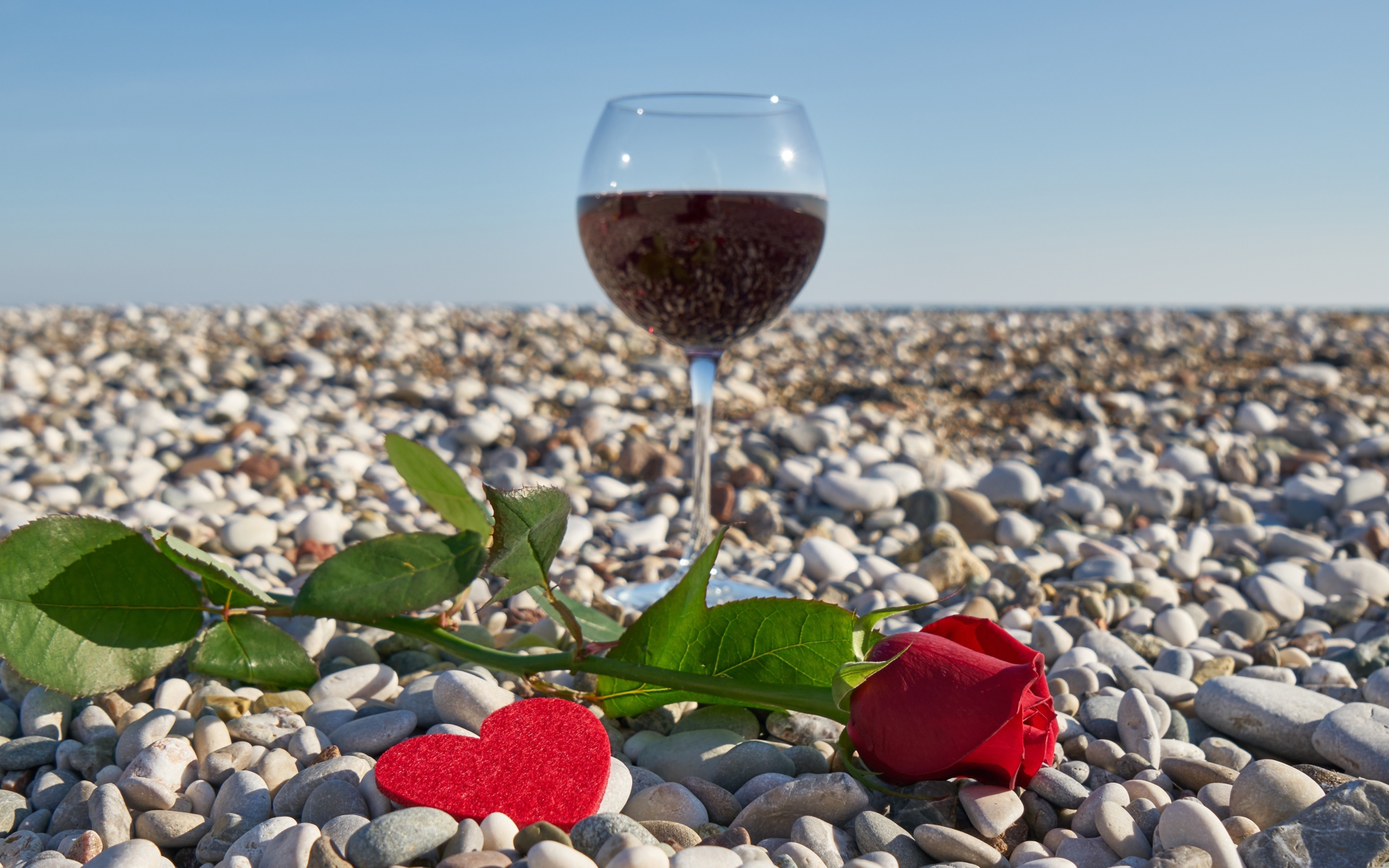 Красная роза на морской гальке с сердечком и бокалом вина